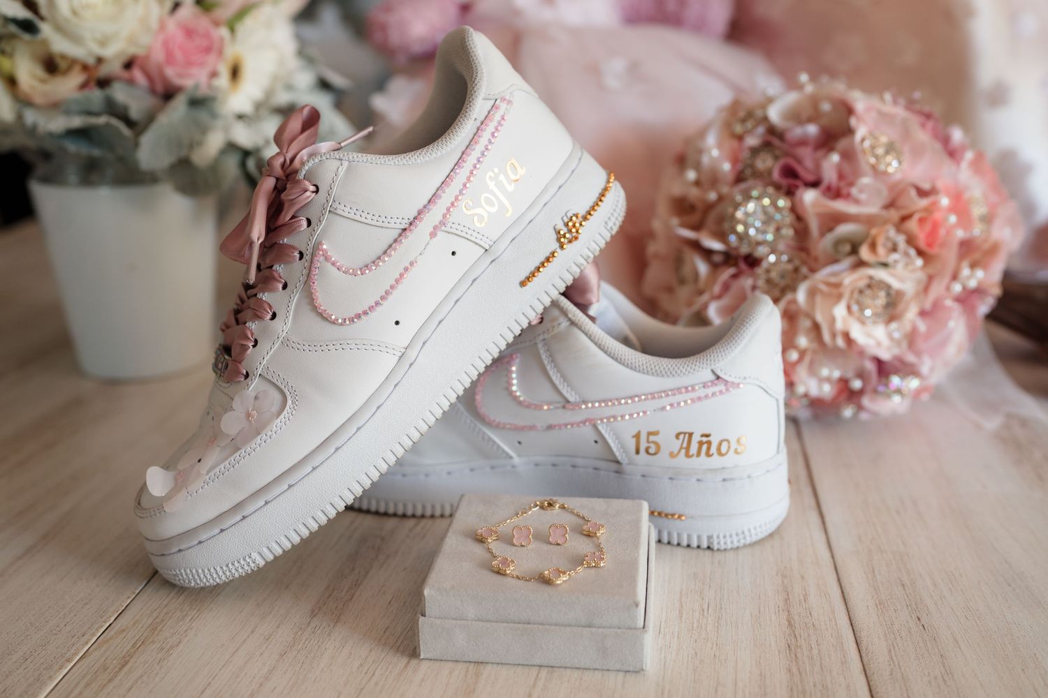 Custom Nike Air Force 1 sneakers with gold '15 Anos' quinceañera embroidery displayed with jewelry and pink floral bouquet.