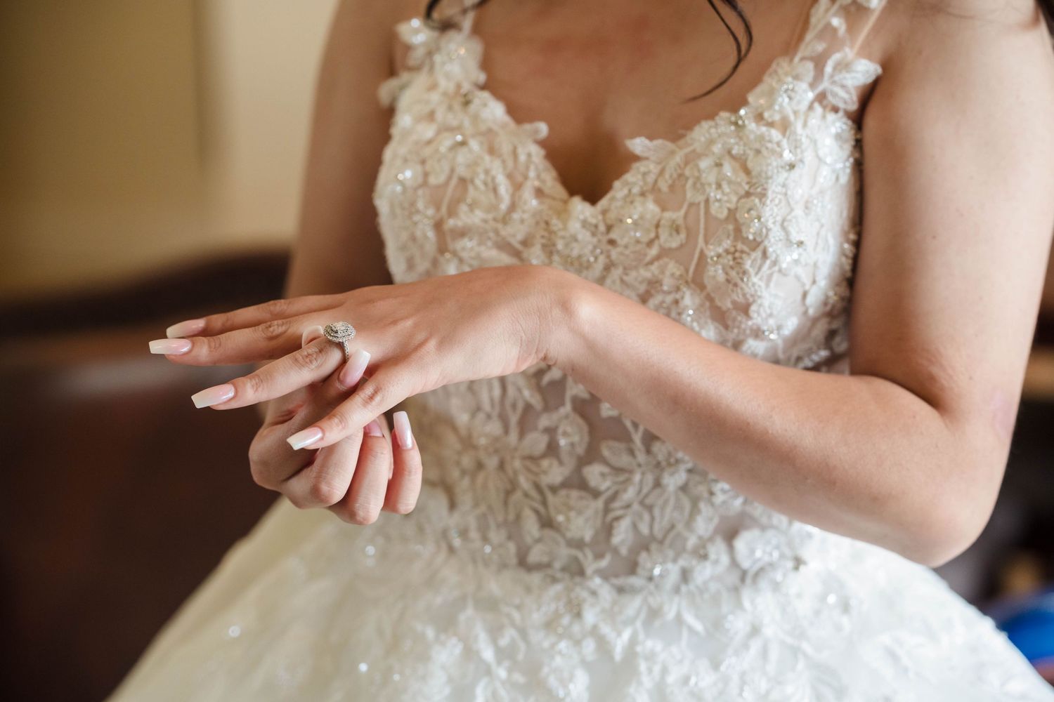 Bride in lace wedding gown adjusting diamond engagement ring on her finger before the ceremony.