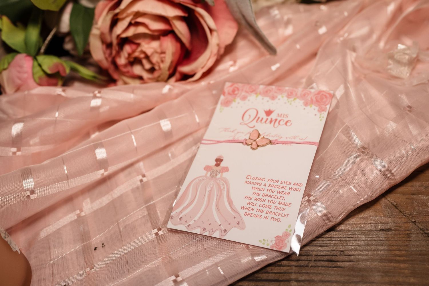 Pink quinceañera invitation card with bell design resting on pink fabric with roses.