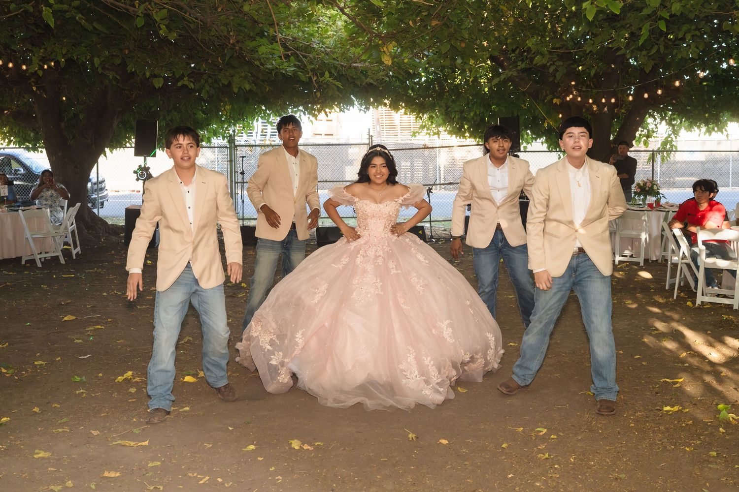 Young woman in pink quinceañera ball gown poses with four men in tan blazers and jeans outdoors.