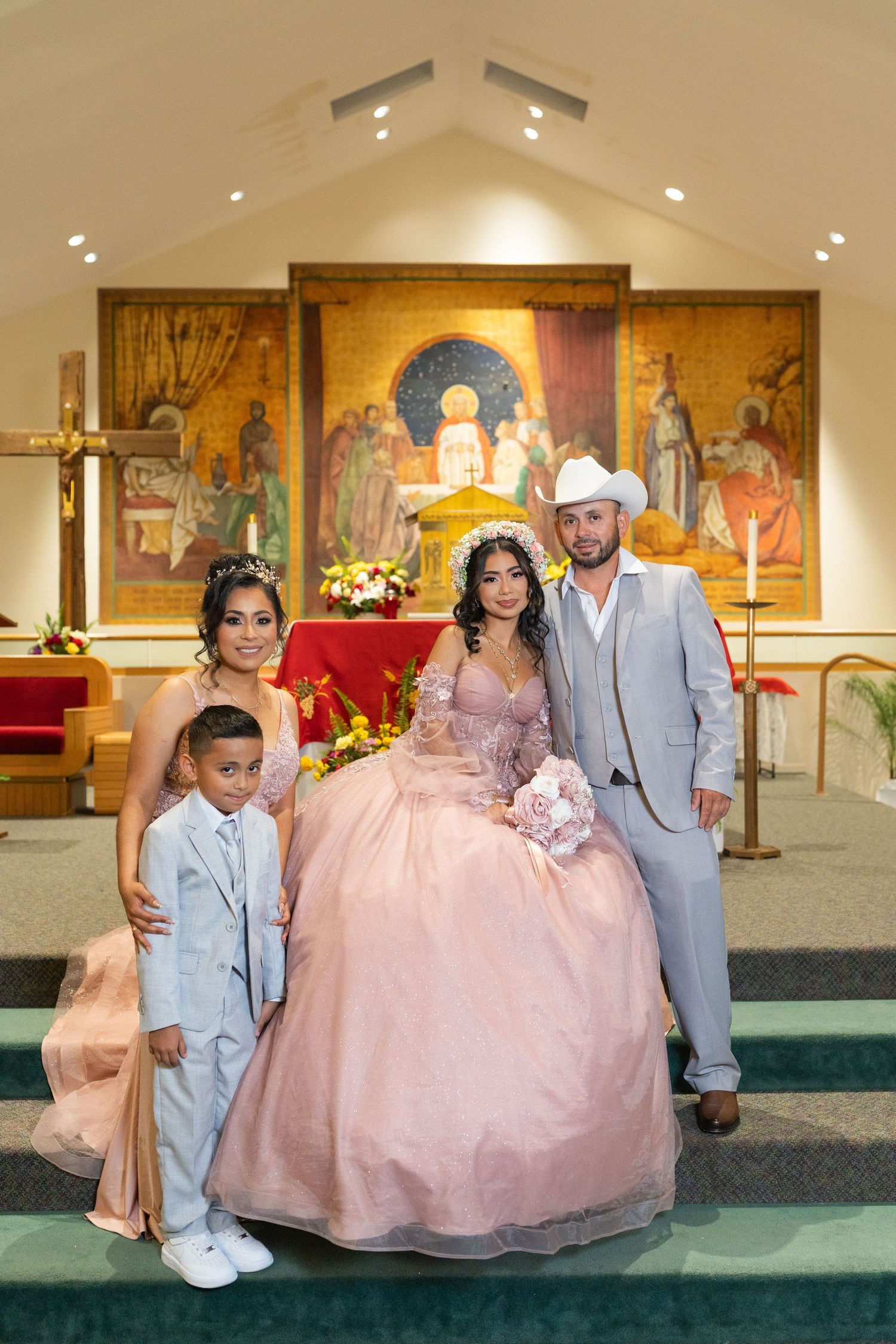 Quinceañera girl in pink gown poses with family at church altar for formal portrait.