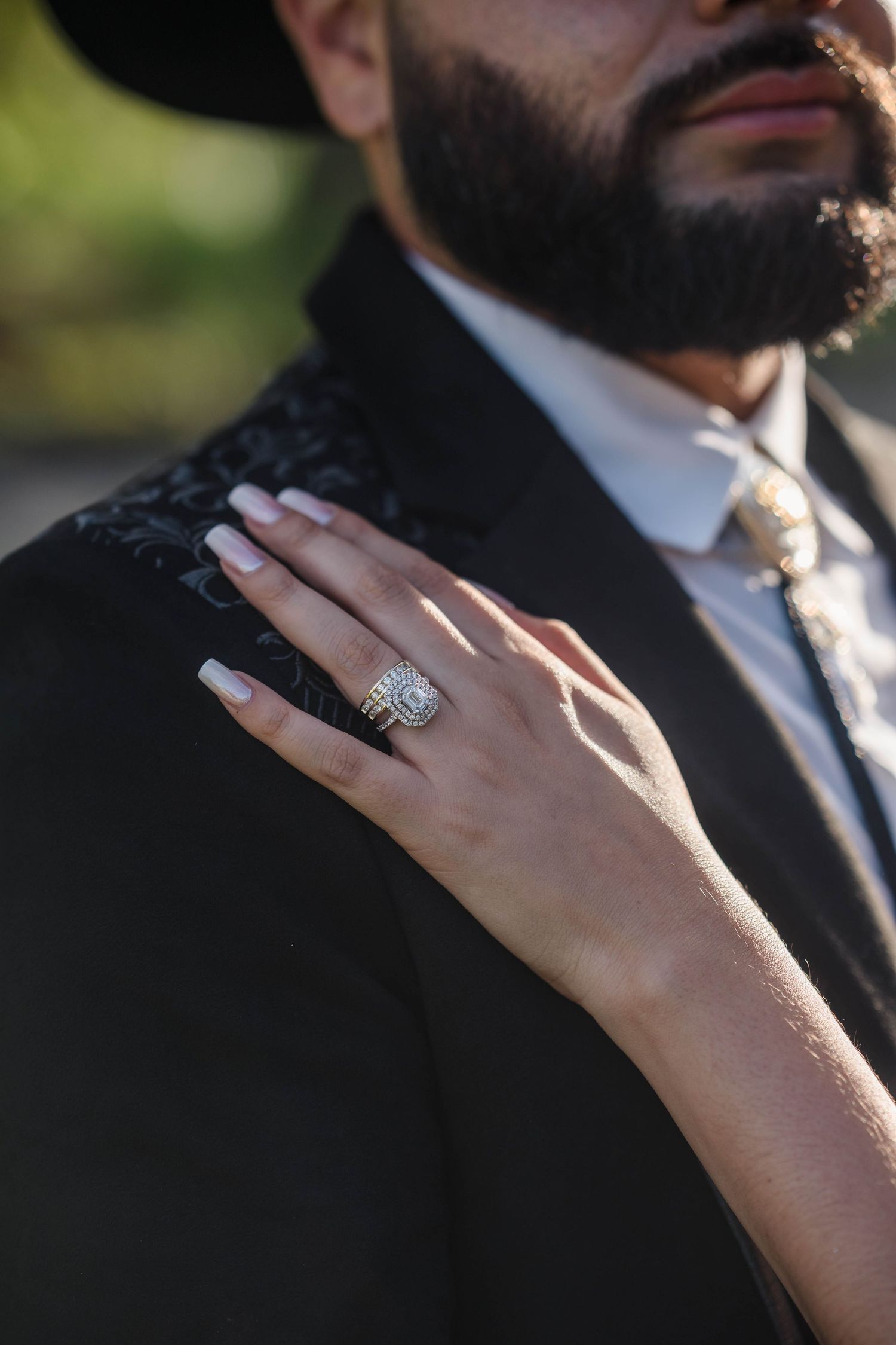 Close-up of bride's hand with diamond wedding ring resting on groom's black suit jacket.