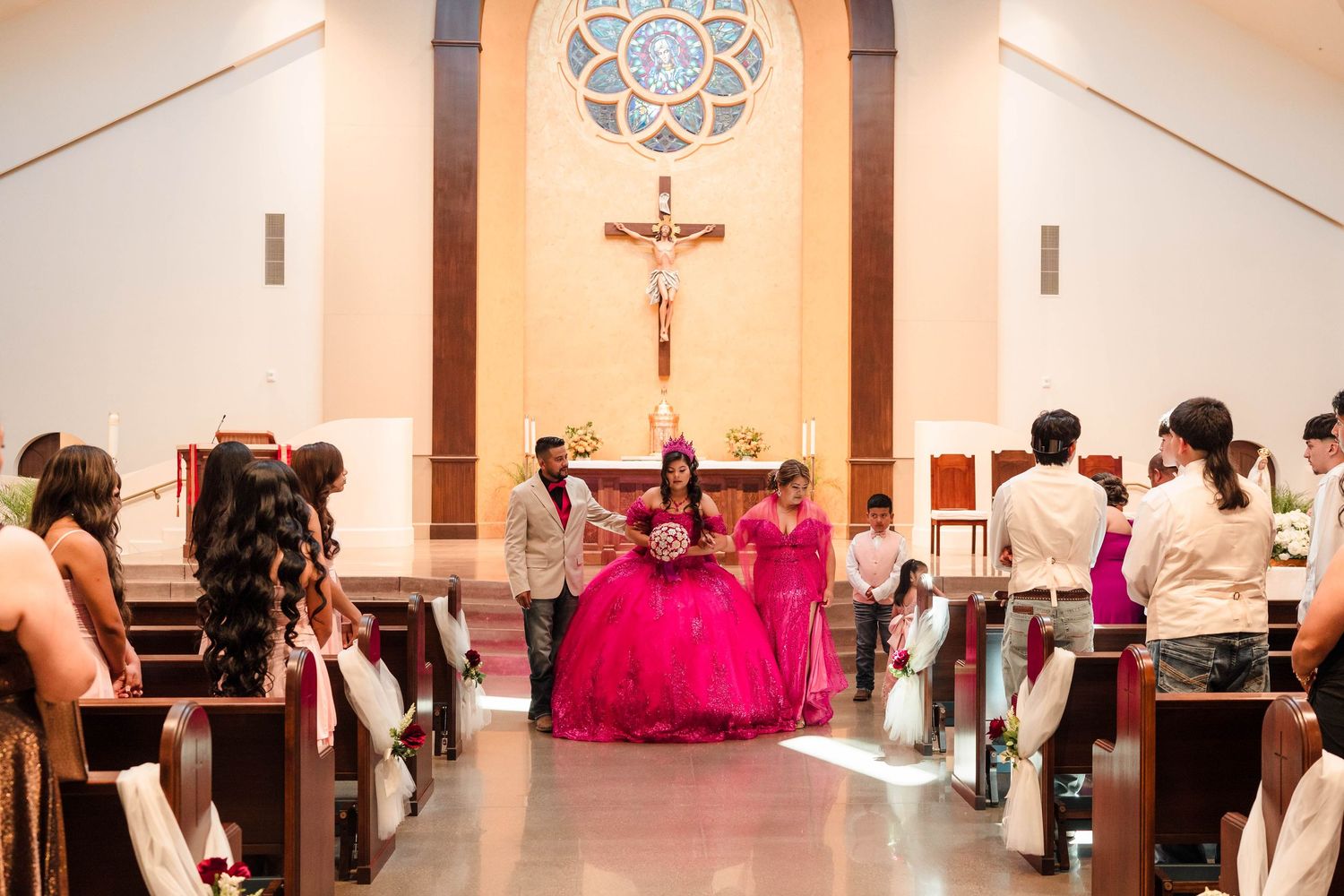 Quinceañera girl in pink ball gown walking down church aisle with escort during ceremony.