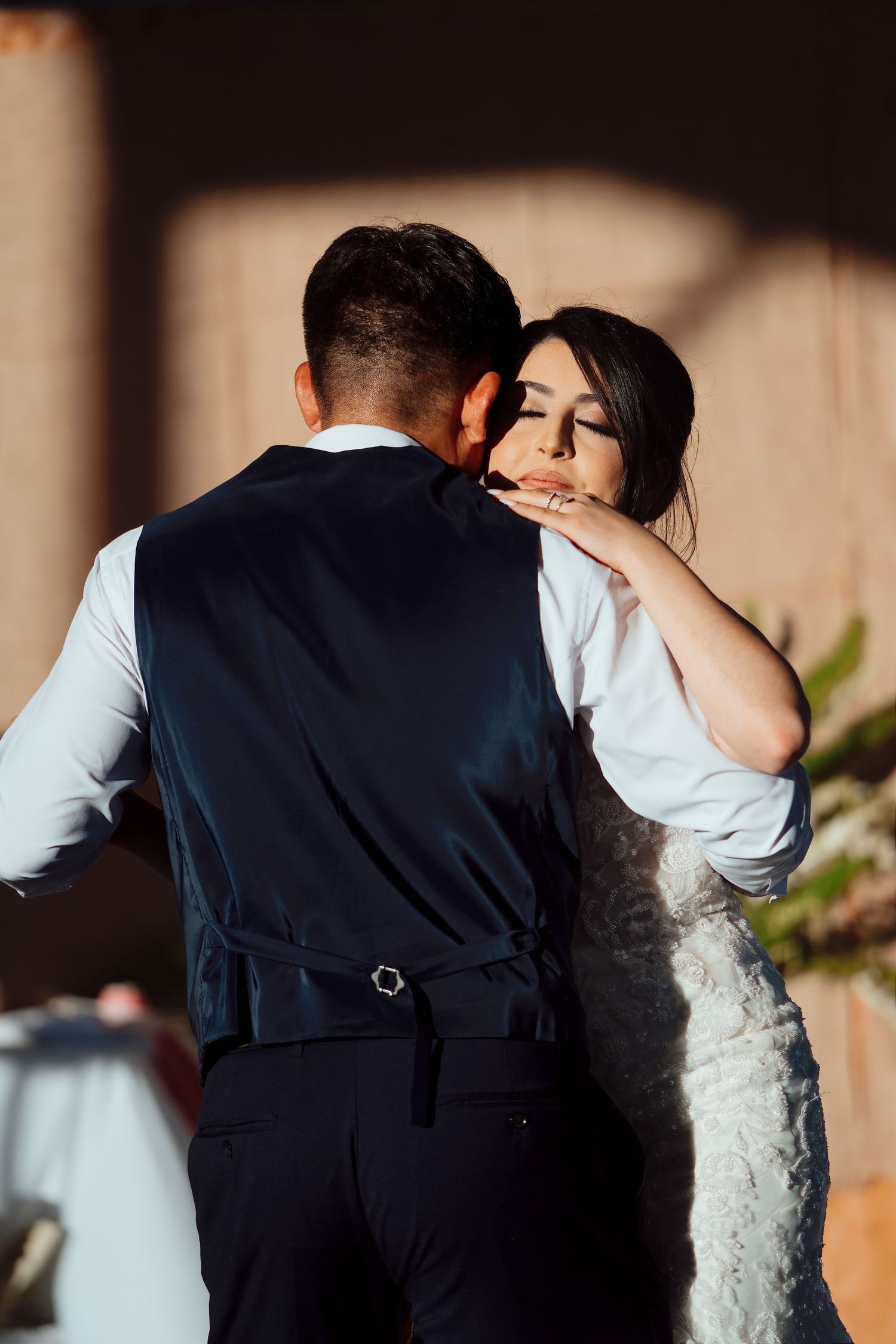 Bride and groom share intimate first dance moment, bride in lace dress rests head on groom's shoulder.