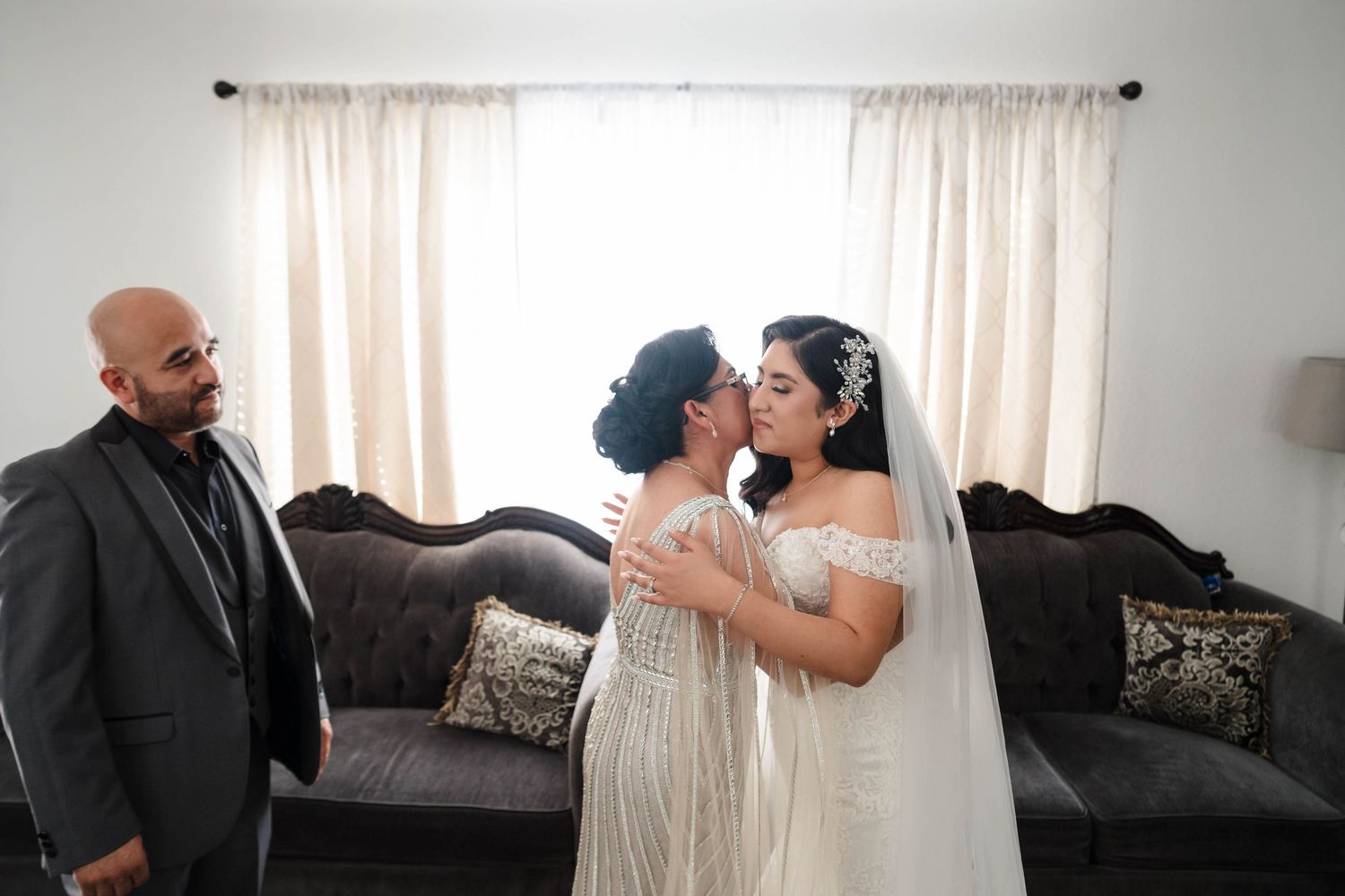 Bride sharing tender kiss with loved one in white gown and veil before wedding.