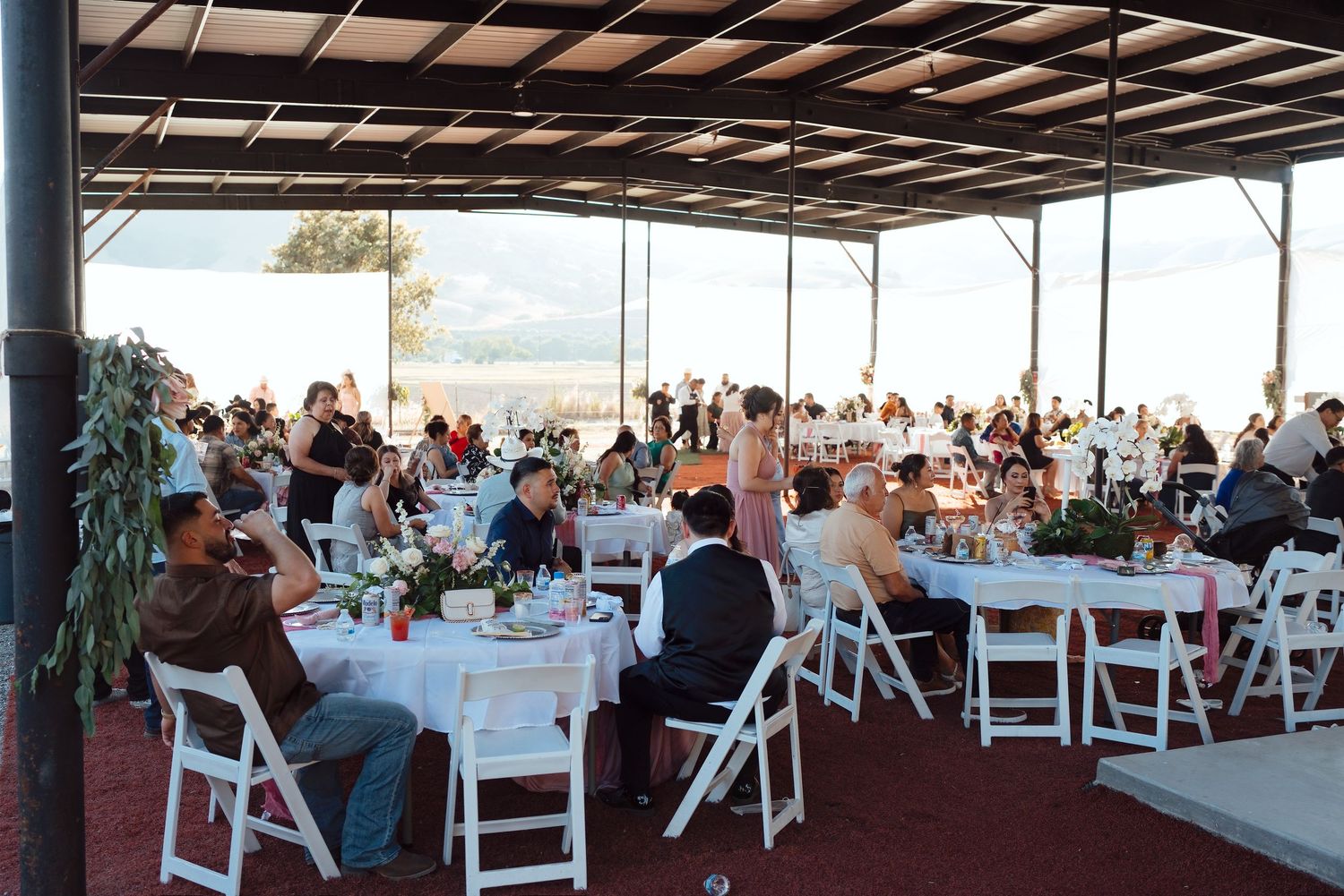 Guests seated at round tables with white chairs at a large outdoor wedding reception venue.