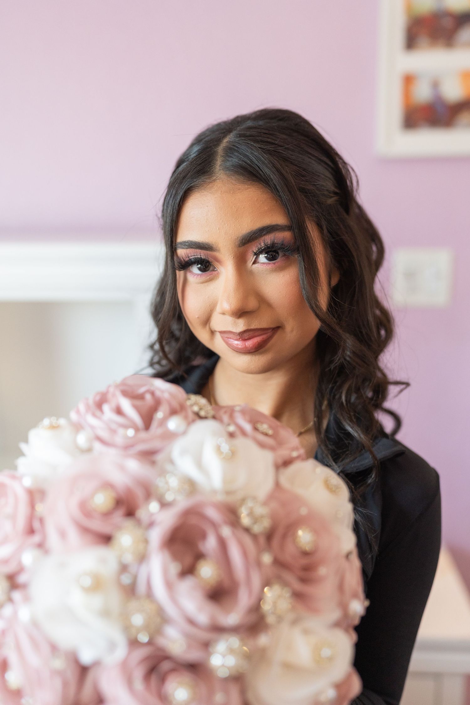 Young woman with dark curly hair holding a bouquet of pink and white fabric roses adorned with pearls.