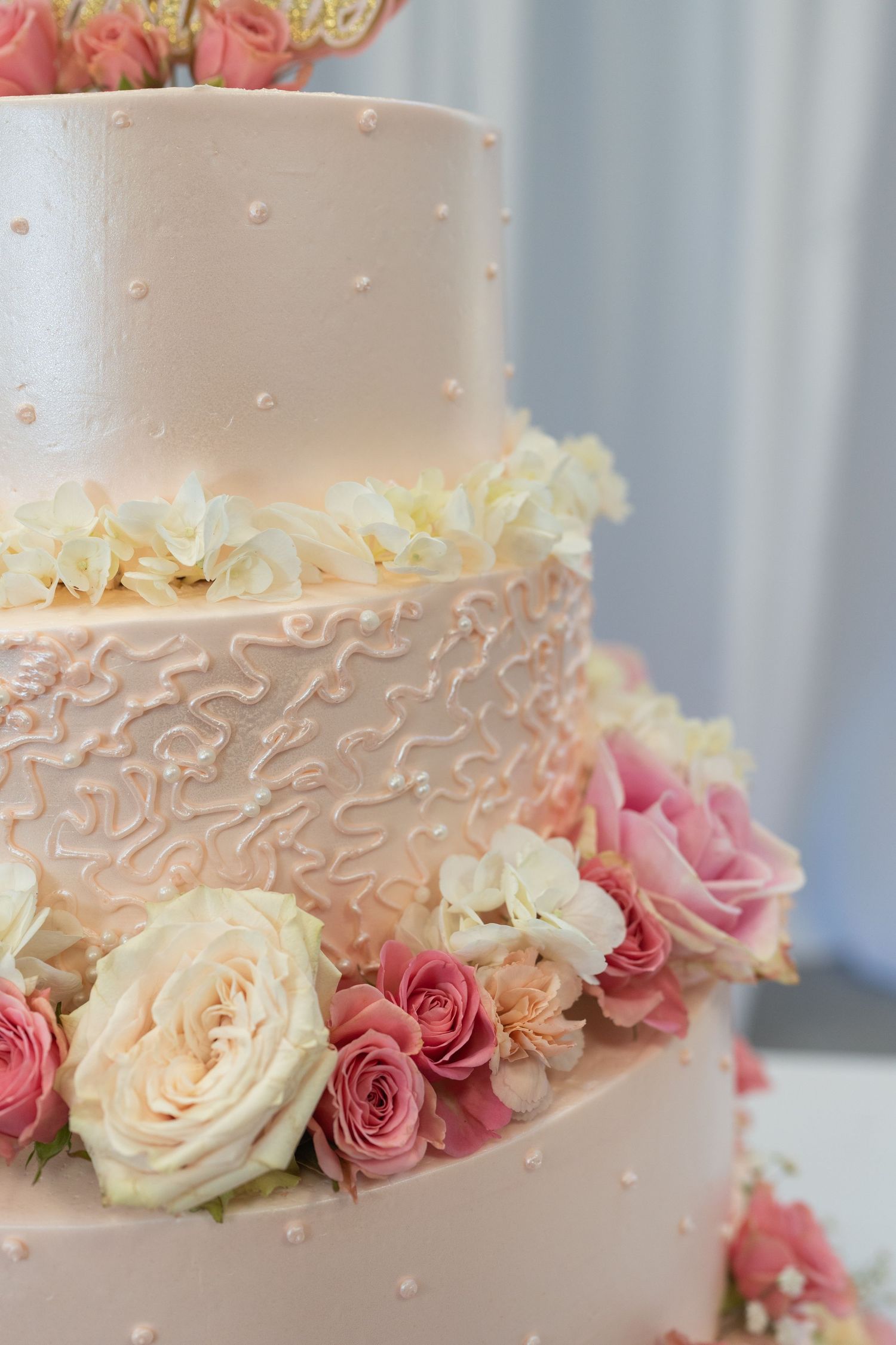 Elegant three-tier pink wedding cake decorated with fresh roses and intricate frosting details.