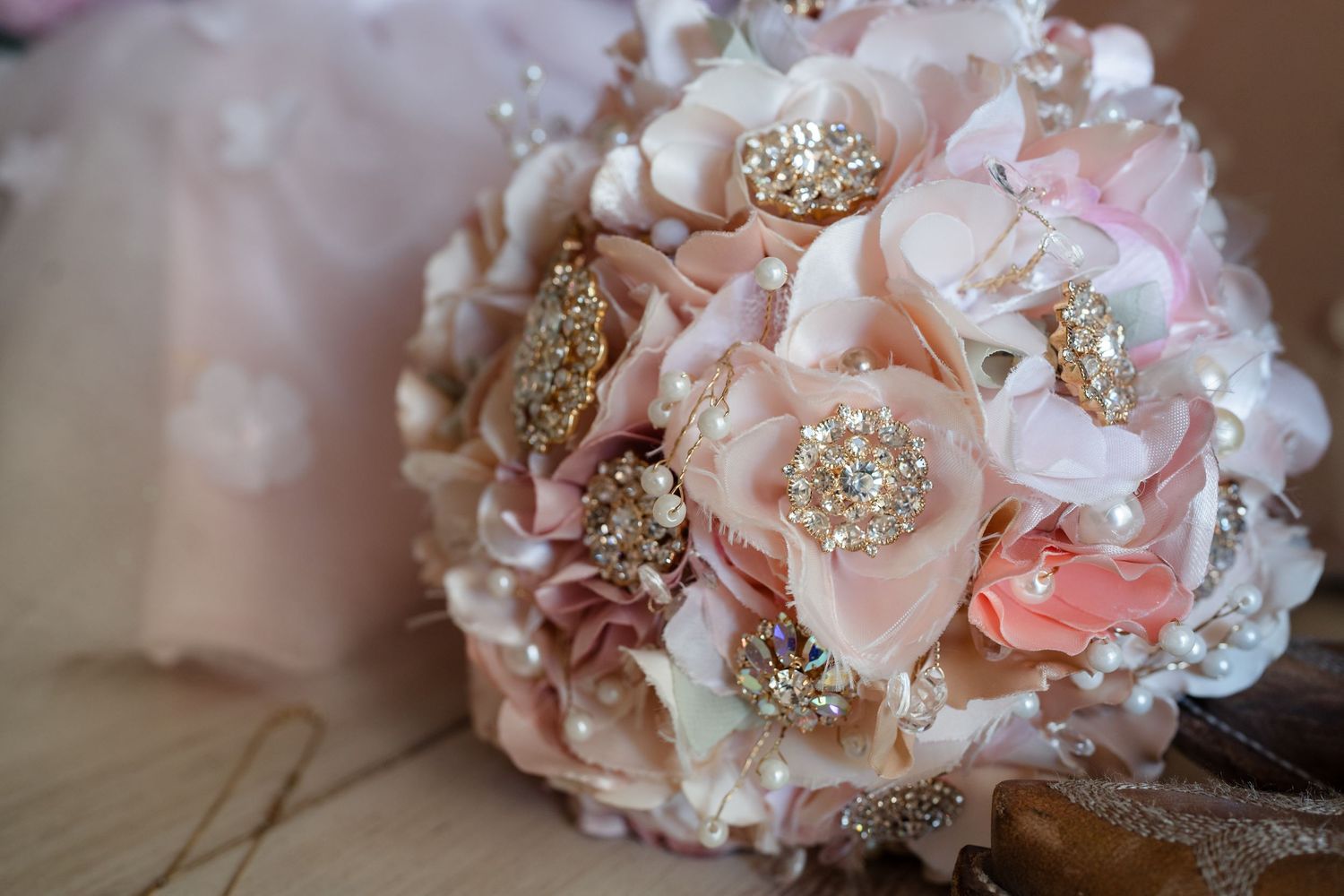 Elegant bridal brooch bouquet with blush pink fabric flowers, gold rhinestone brooches, and pearl embellishments.