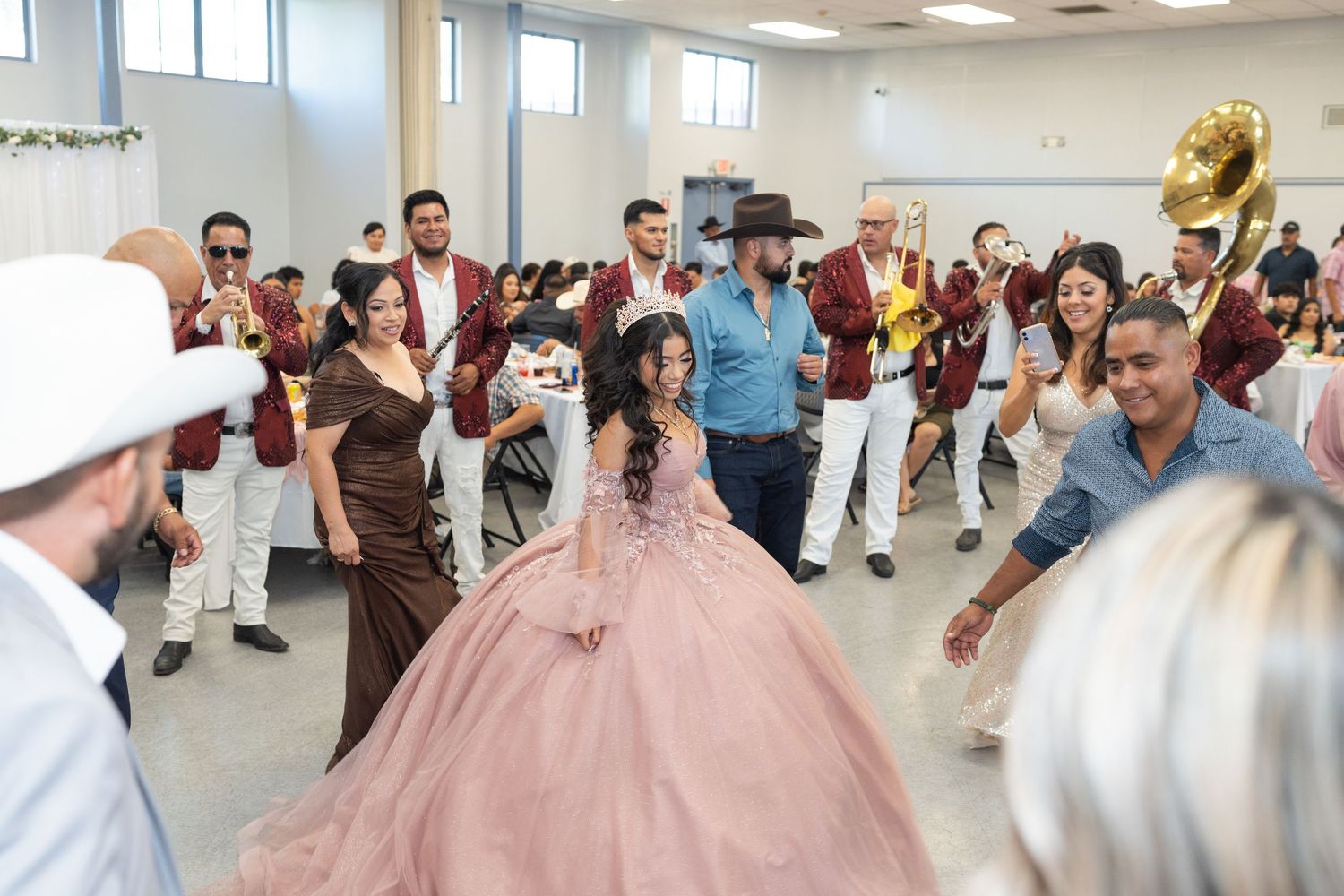 Quinceañera girl in pink ballgown dances surrounded by a live band and guests at her party.