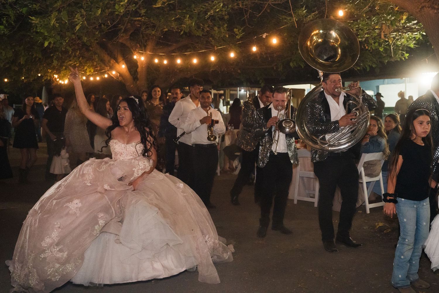 A quinceañera dances in a pink ball gown while a brass band performs at her outdoor celebration.
