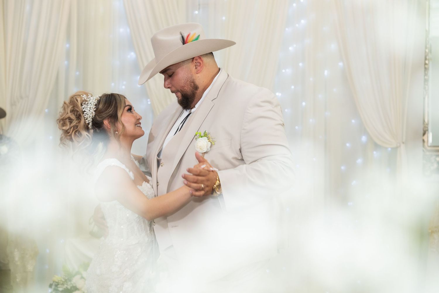 Bride and groom share first dance at elegant wedding reception with twinkling lights backdrop.