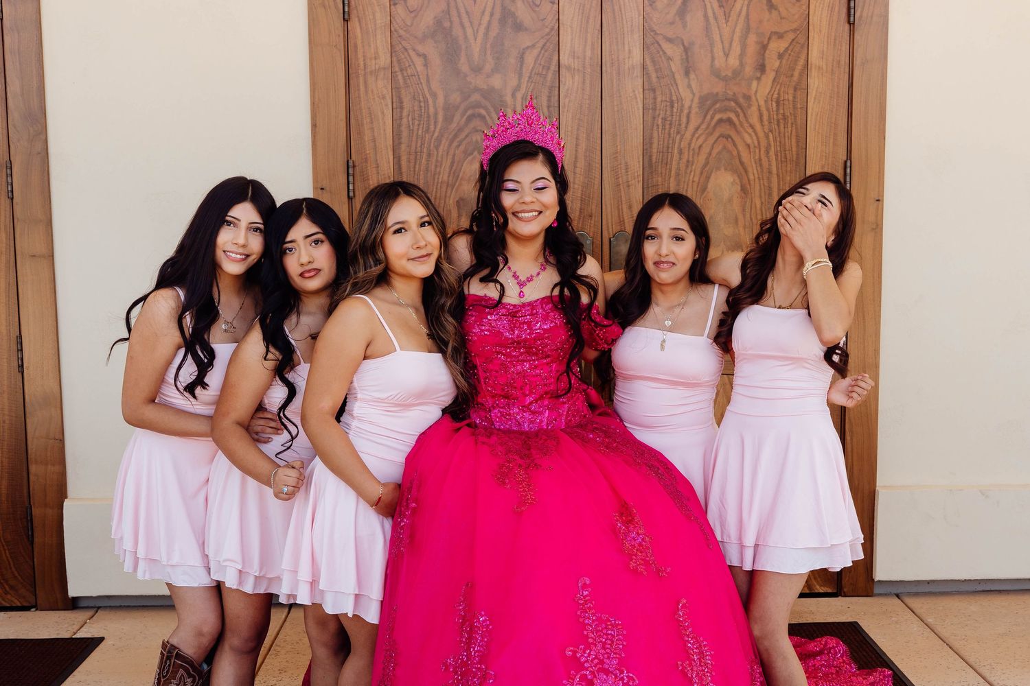 Quinceañera girl in hot pink gown smiles with bridesmaids in light pink dresses at celebration.