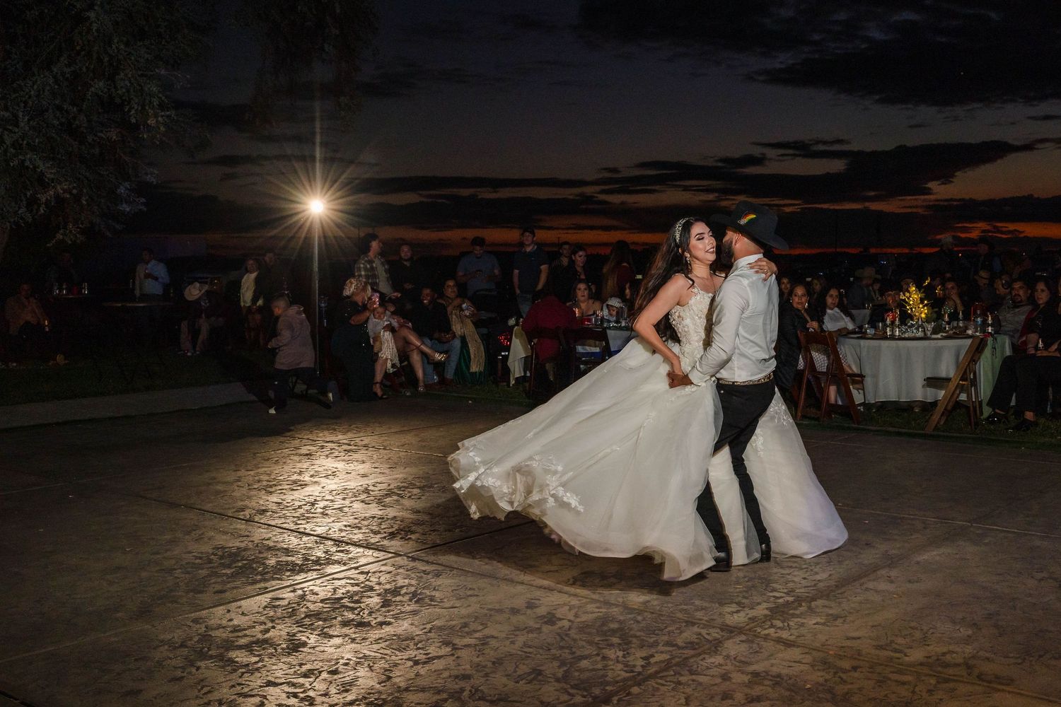 Bride and groom share a romantic first dance outdoors at sunset, with the bride's white gown swirling gracefully.