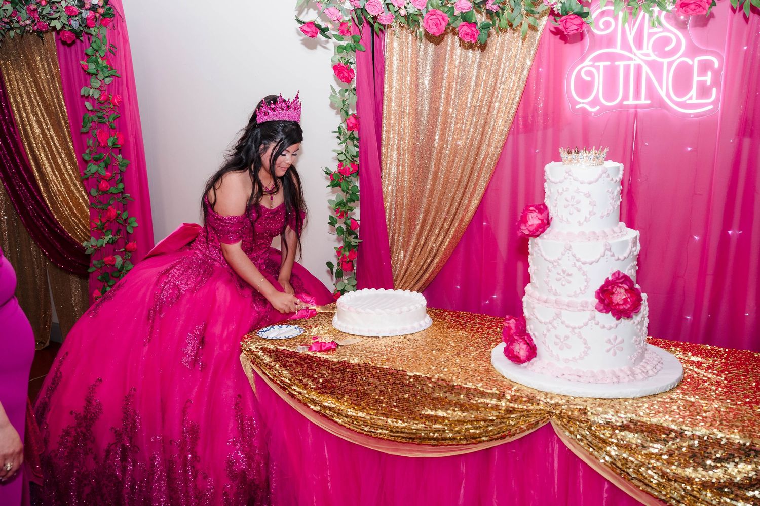 Quinceañera girl in a hot pink ball gown cuts her elegant white tiered cake at her festive celebration.