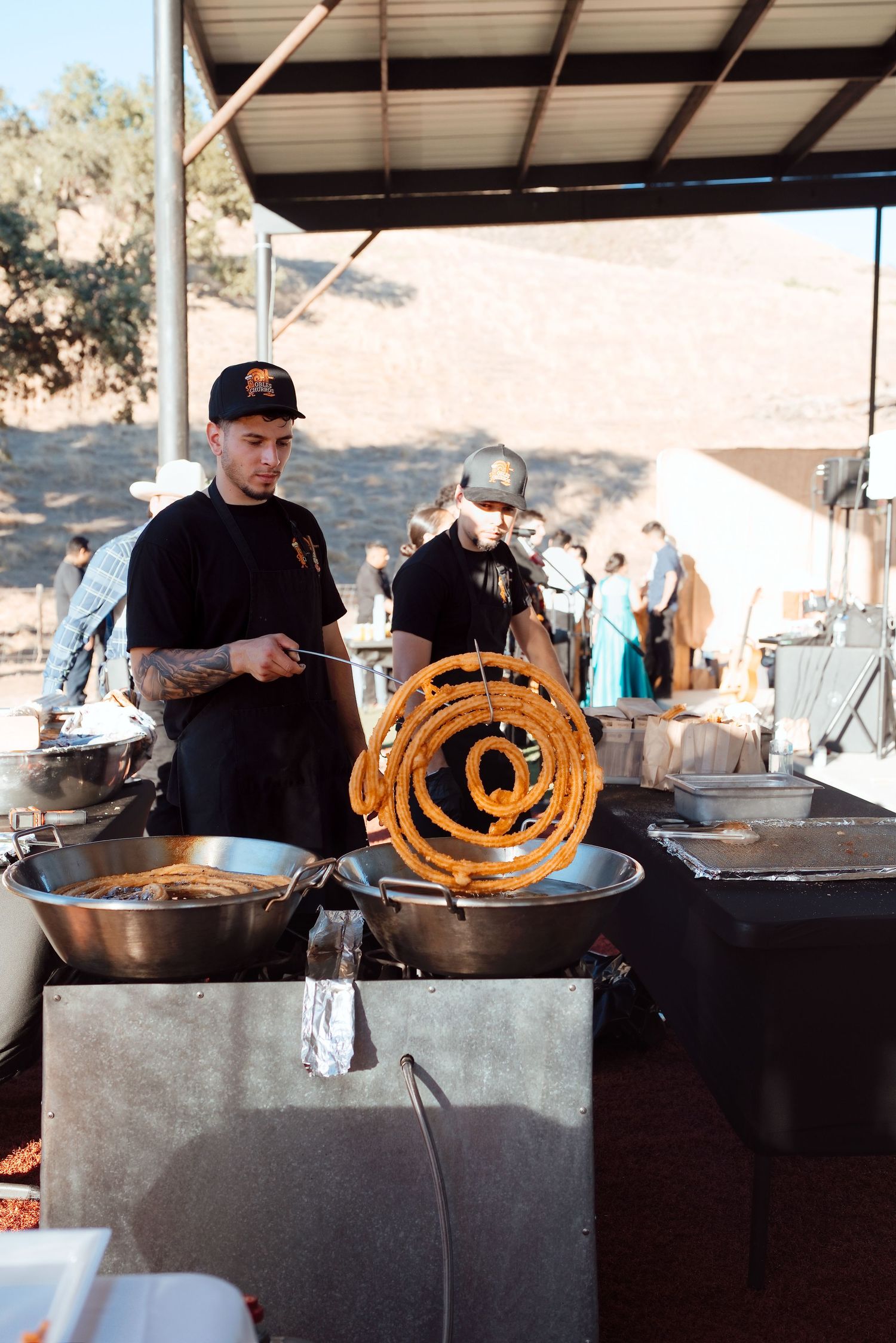 Chef frying spiral churros at an outdoor food stall with large pans at a sunny festival event.