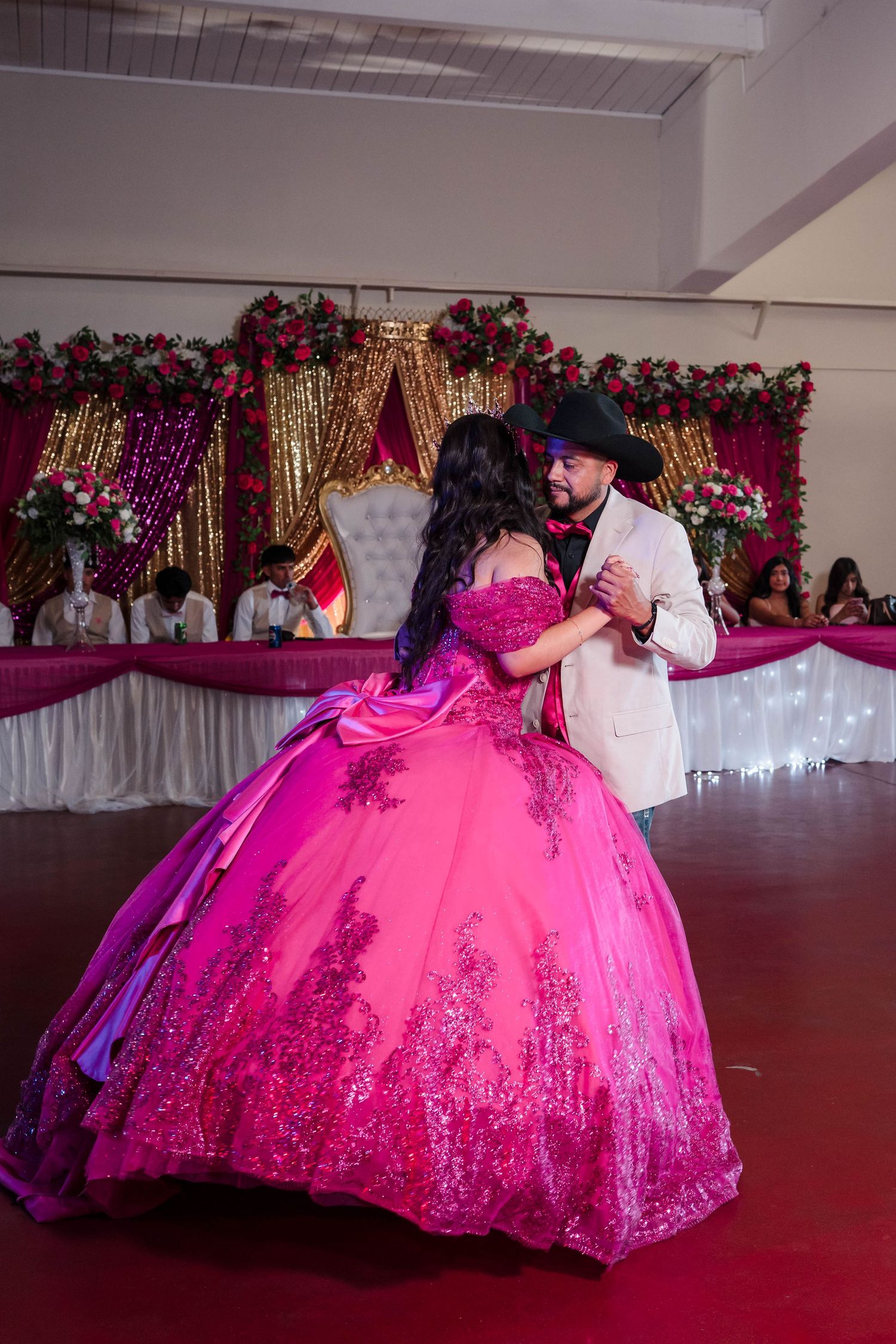 Father and daughter share a touching waltz dance at a quinceañera reception with pink floral decor.