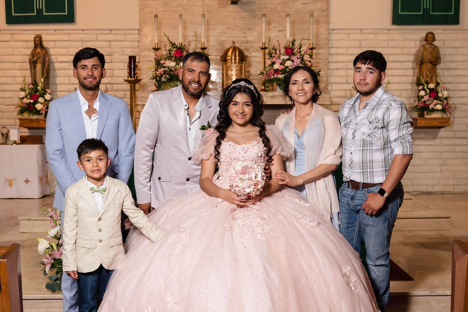 A girl in a pink quinceañera ball gown poses with family members inside a decorated church.