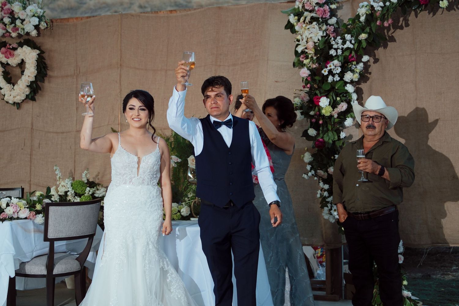 Bride and groom raising champagne glasses in a toast at their elegant wedding reception with floral decorations.
