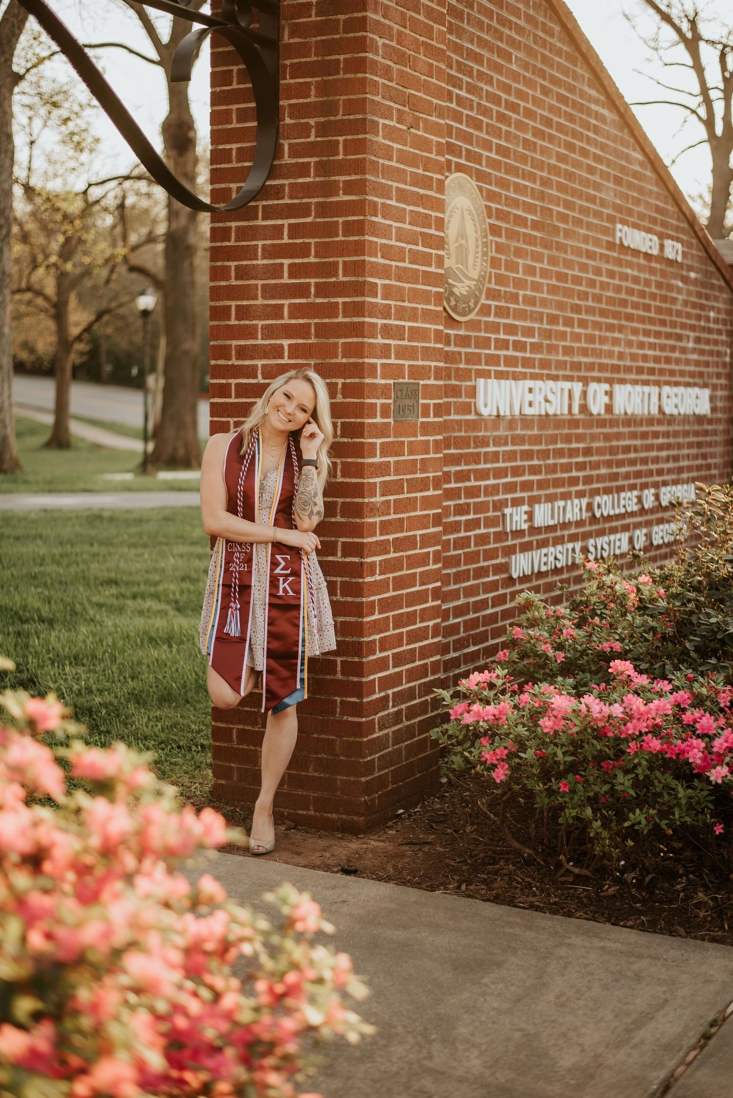 Blonde female graduate wearing Sigma Kappa stole posing beside University of North Georgia brick sign.