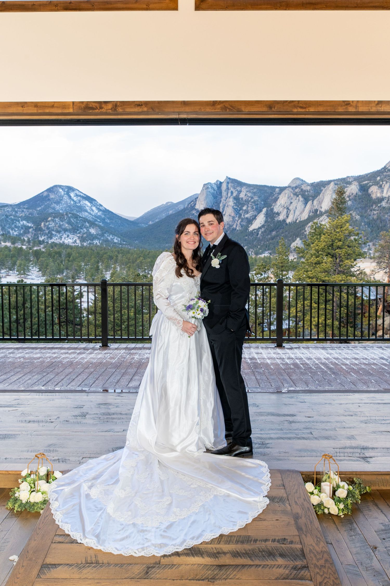 Bride and groom pose at mountain wedding venue with snowy Rocky Mountain backdrop on overcast winter day.
