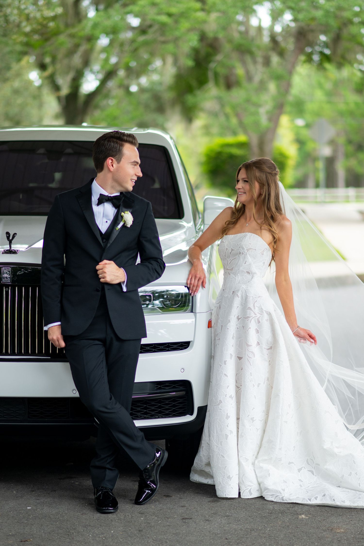 Bride and groom posing elegantly beside a white Rolls-Royce on their wedding day.
