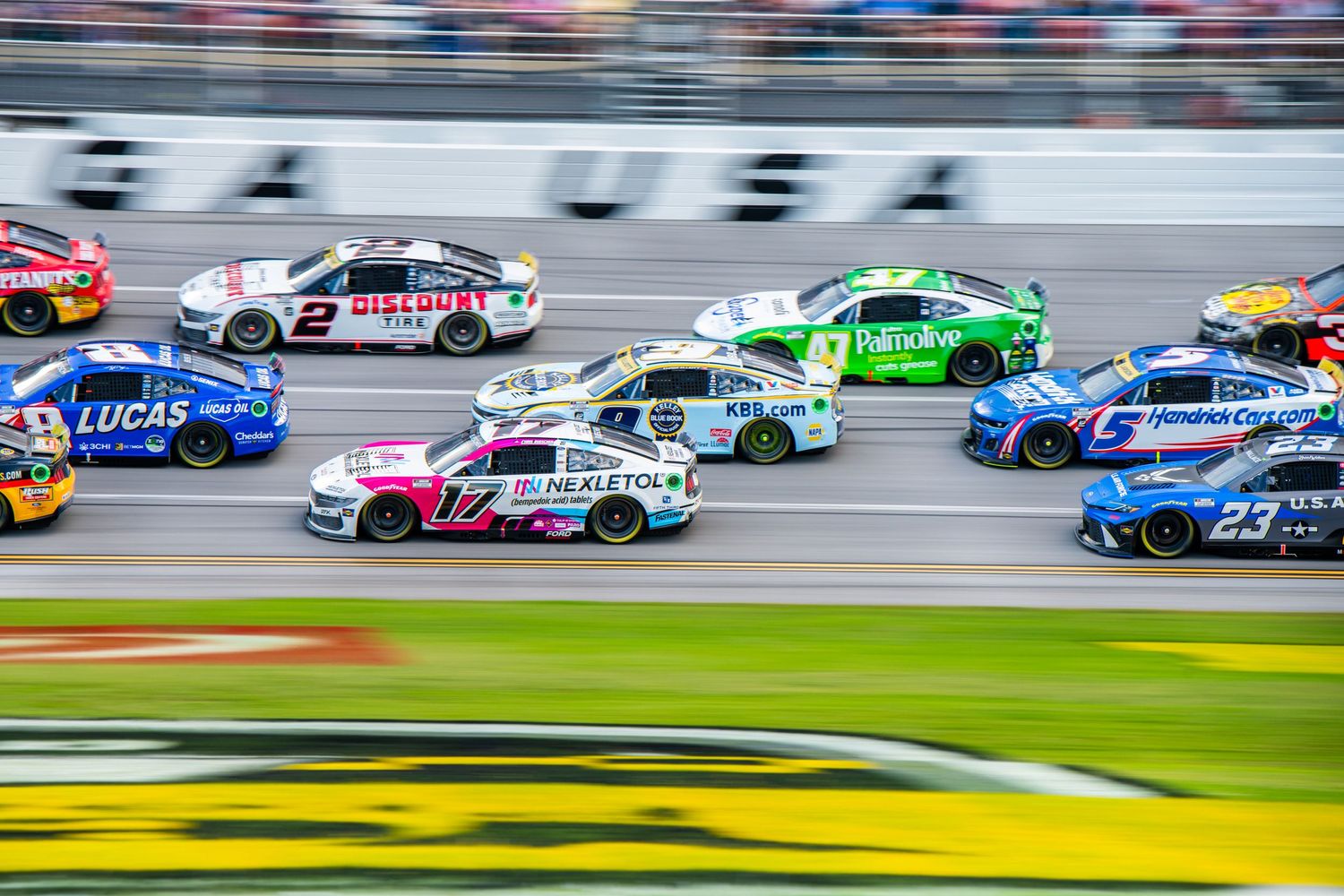 Pack of NASCAR Cup Series cars racing side by side at Talladega Superspeedway.