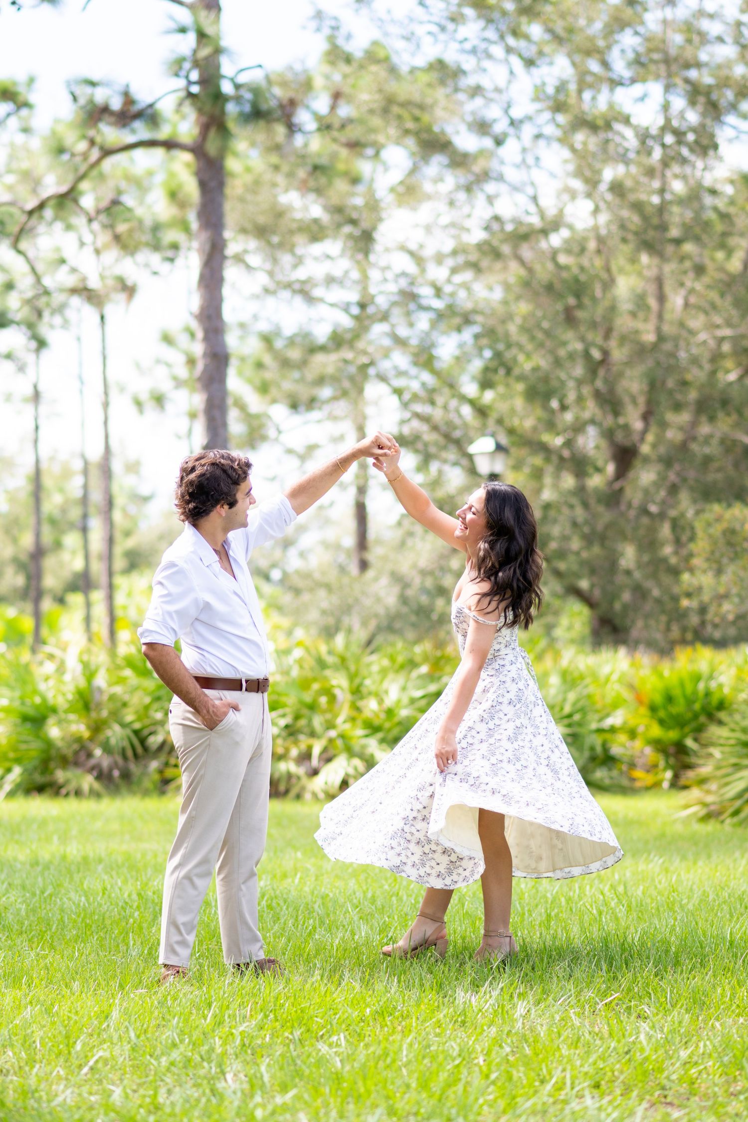 Joyful couple dancing together on lush green lawn surrounded by tropical trees and plants.