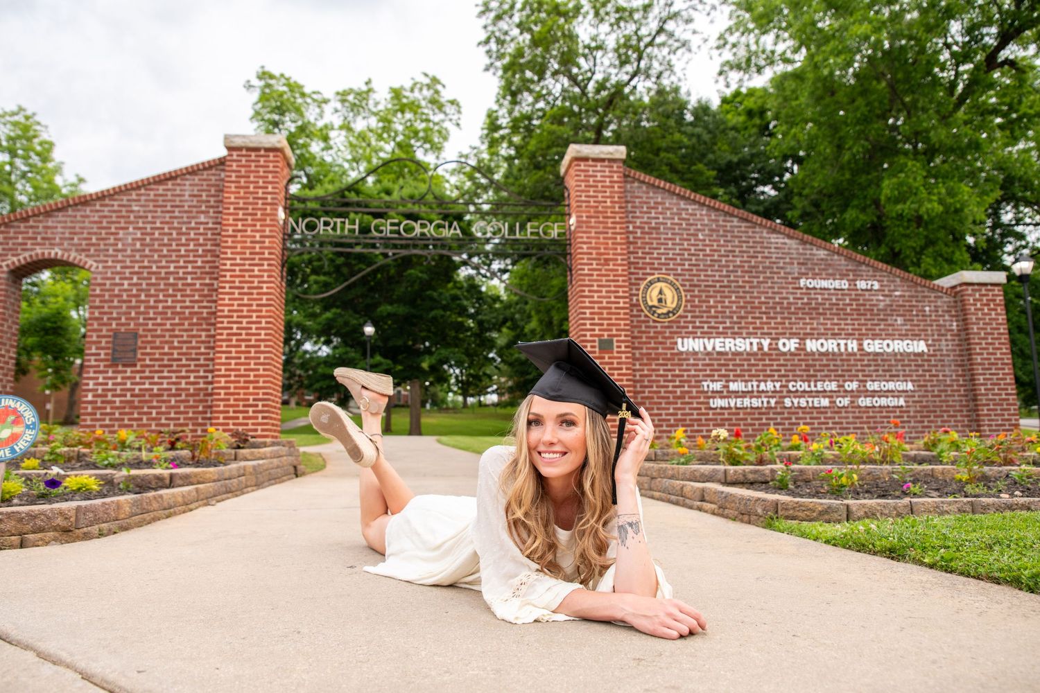 Smiling female graduate in cap and gown posing at University of North Georgia entrance sign.