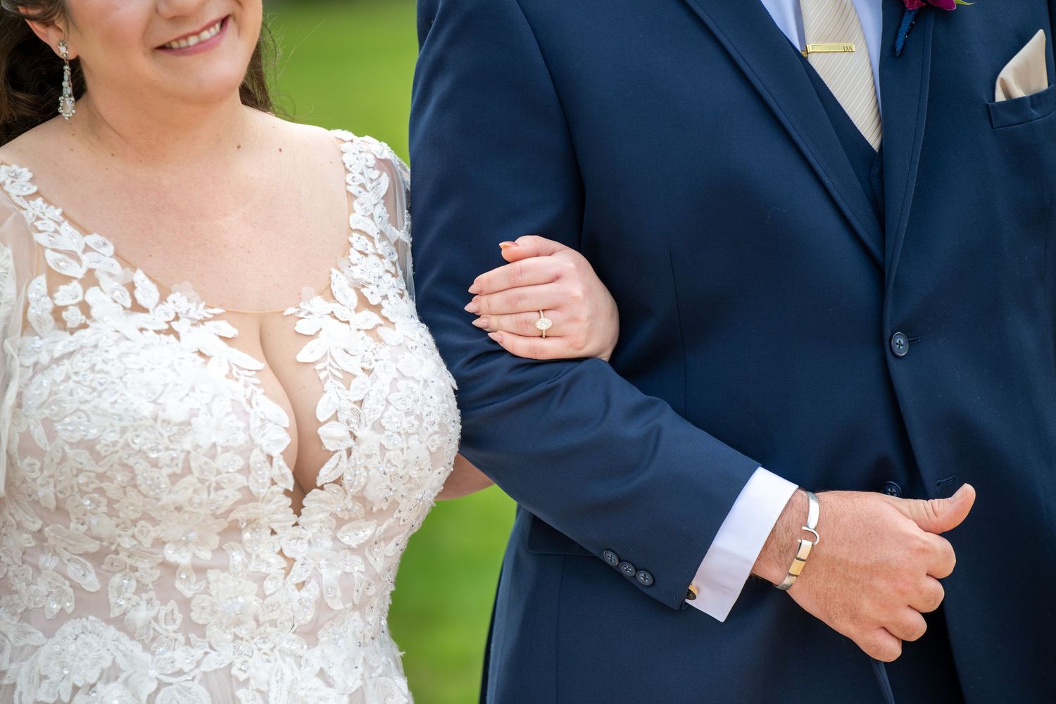 Close-up of bride and groom linking arms, showcasing wedding rings and elegant attire.