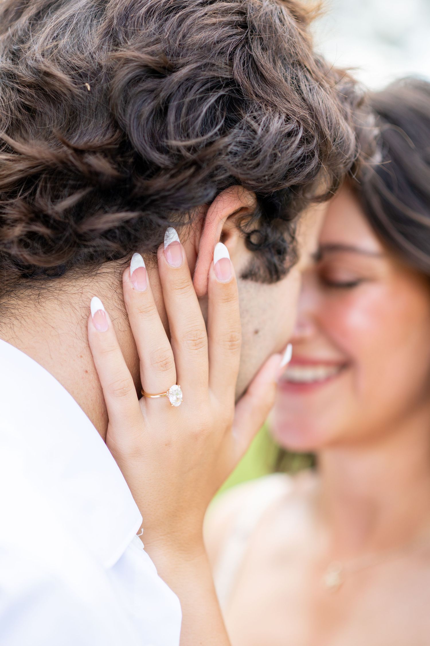 Close-up of smiling bride touching groom's face, showcasing diamond engagement ring with French manicure.