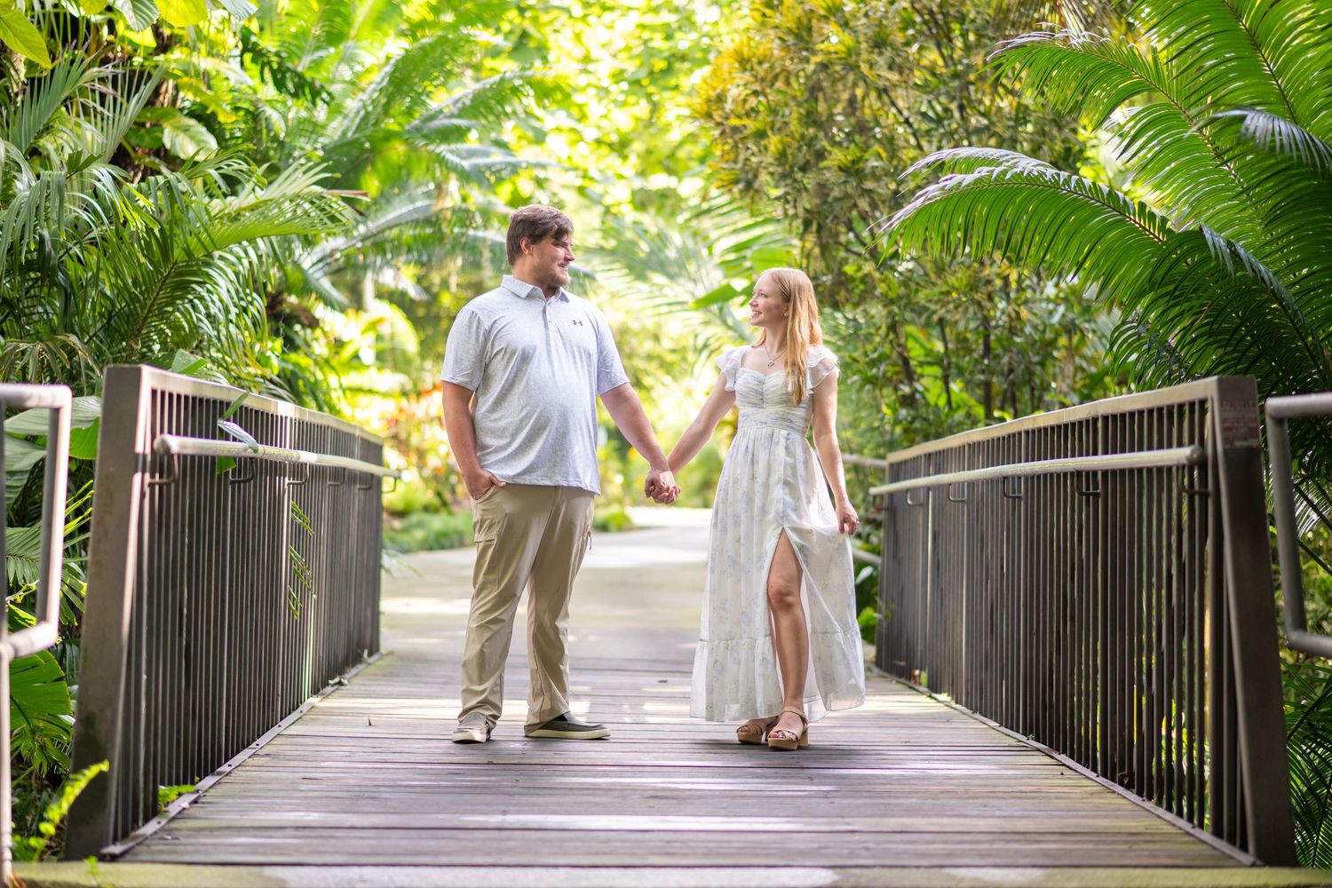 Romantic couple holding hands on a wooden bridge surrounded by lush tropical greenery.