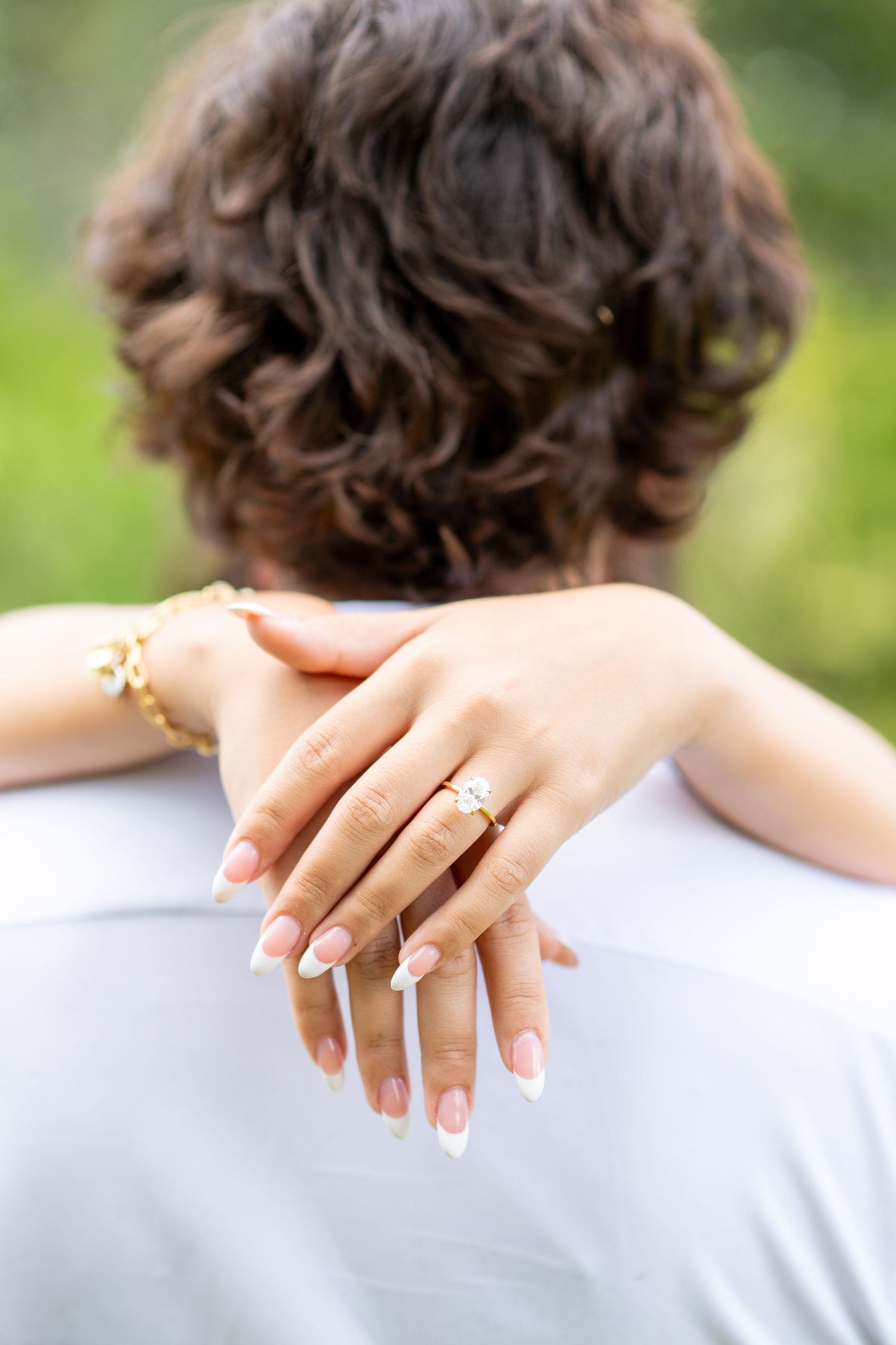 Close-up of woman's hand with engagement ring and gold bracelet resting on man's shoulder.