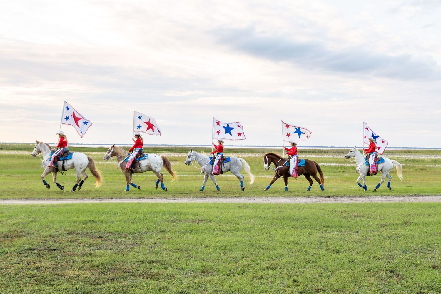 Five riders on horses carrying Panama flags parade across a green field in traditional red and white uniforms.