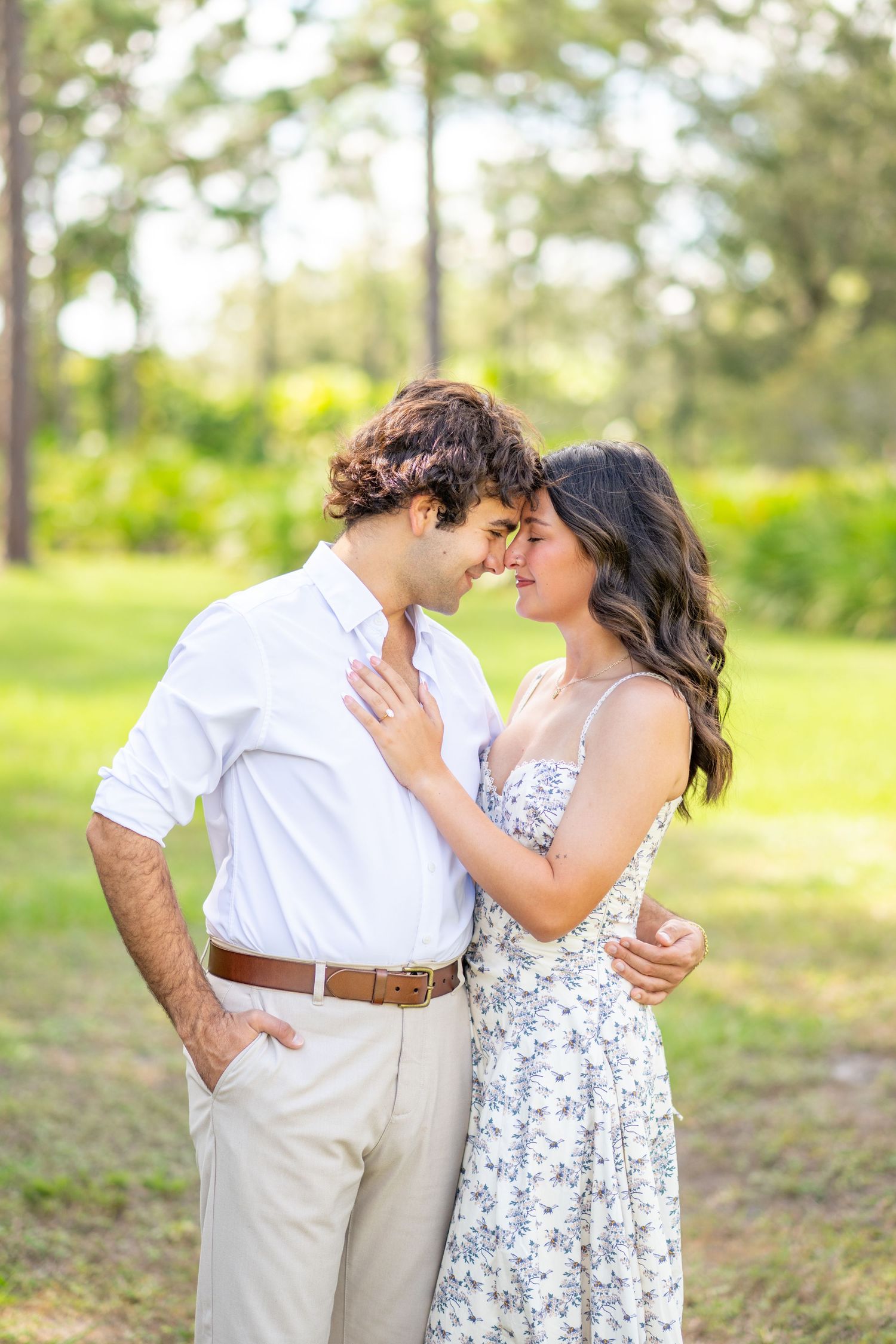 Romantic couple touching foreheads tenderly in a lush green outdoor park during golden hour.