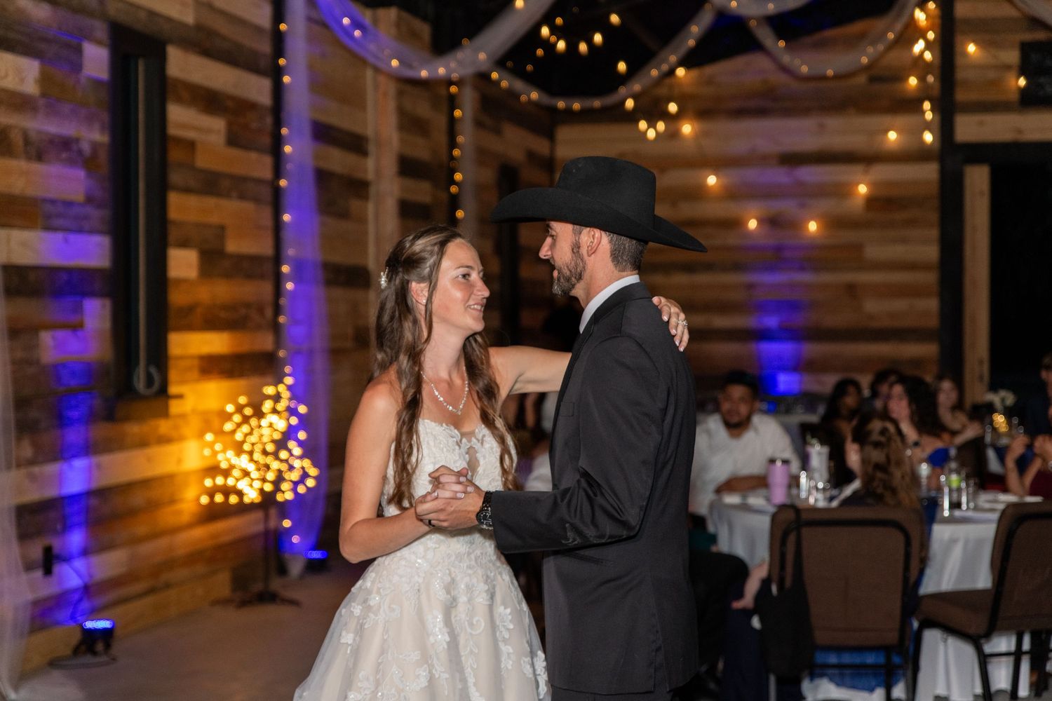 Bride and groom sharing their first dance in a rustic barn with string lights.