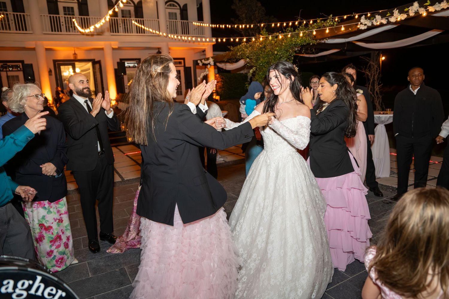 Guests dancing joyfully at an outdoor wedding reception with string lights overhead.