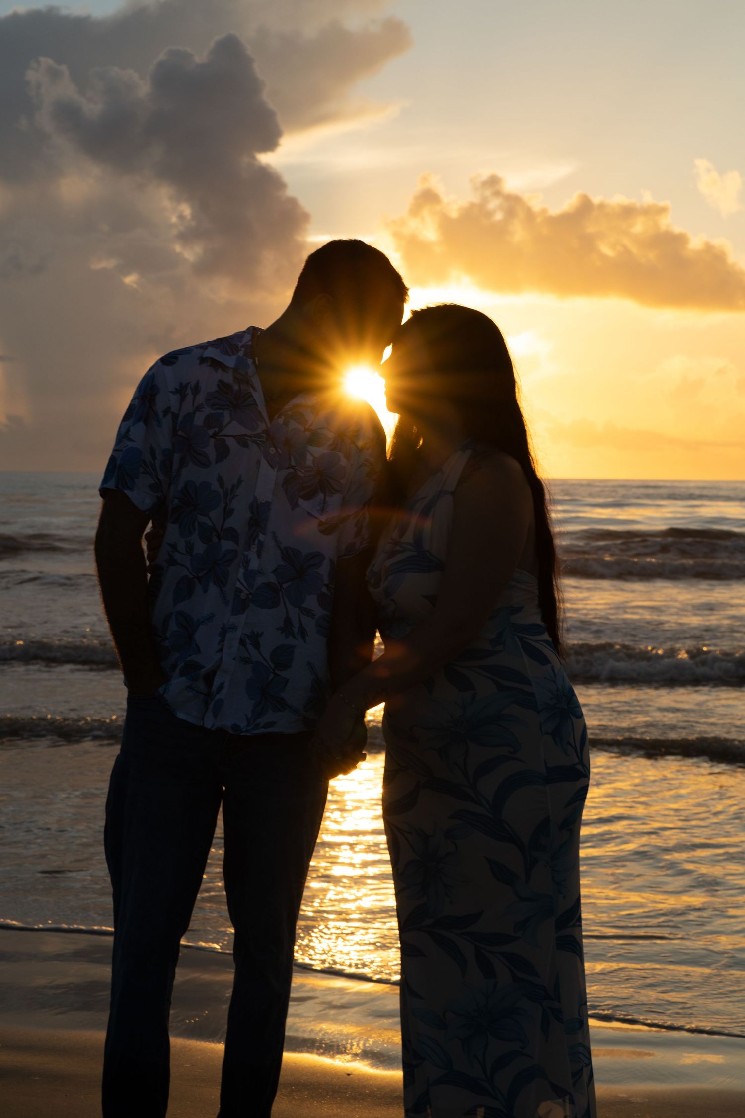 Romantic couple silhouetted against a golden sunset on a beach, sharing an intimate moment with ocean waves behind them.