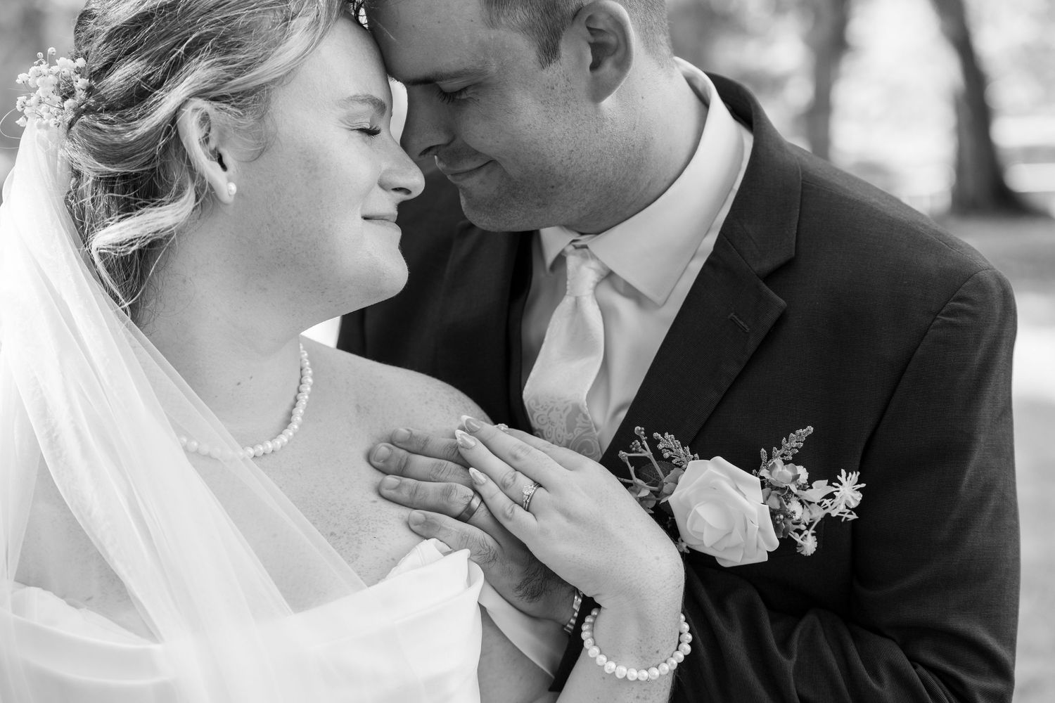 Black and white wedding photo of bride and groom sharing a tender moment, bride wearing veil and pearl jewelry.