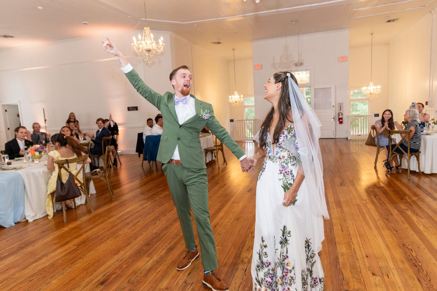 Bride and groom making a joyful entrance onto the dance floor at their elegant white wedding reception.