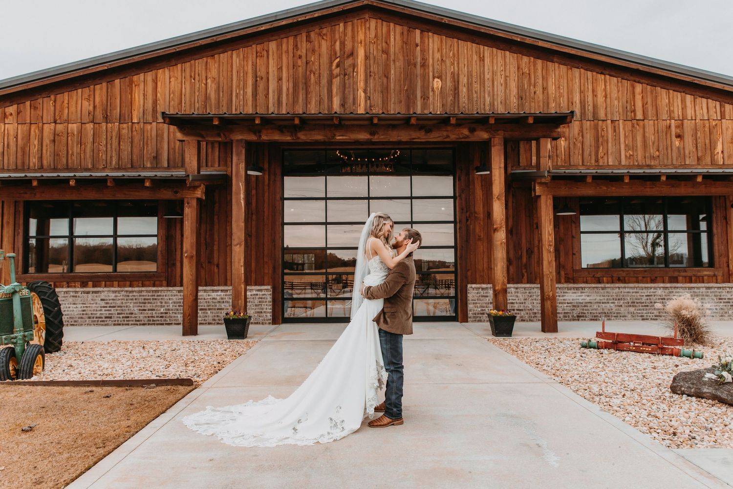 Bride and groom embrace in front of a rustic wooden barn wedding venue on a romantic outdoor celebration.