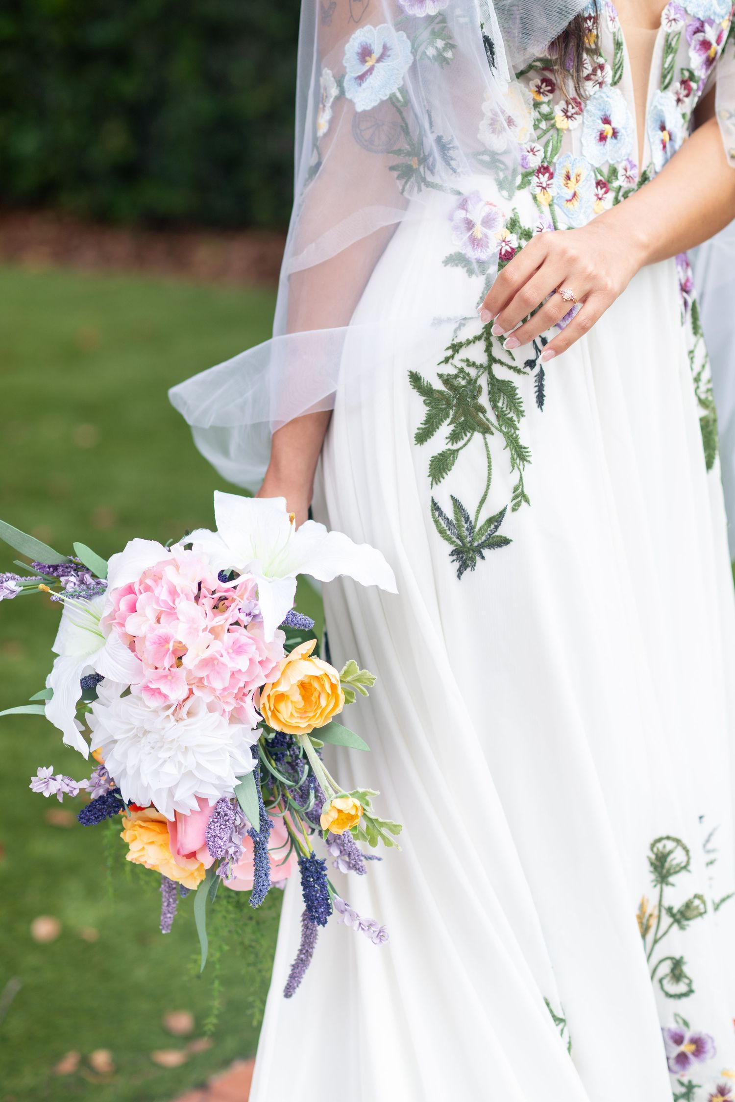 Bride in floral embroidered white wedding gown holding a colorful bouquet of pink, white, and yellow blooms.