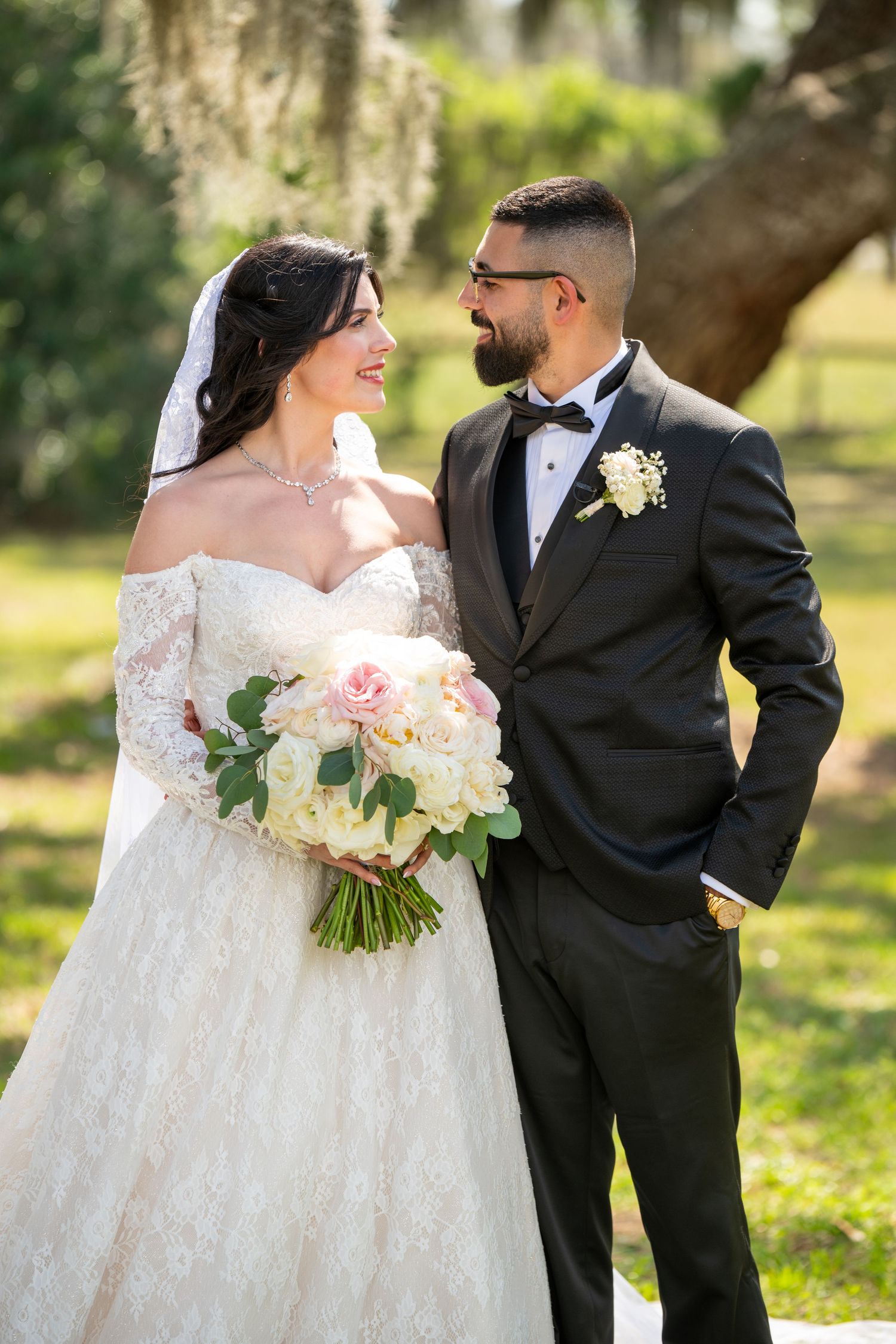 Bride and groom share a loving glance outdoors, bride holding a pink and white bouquet.