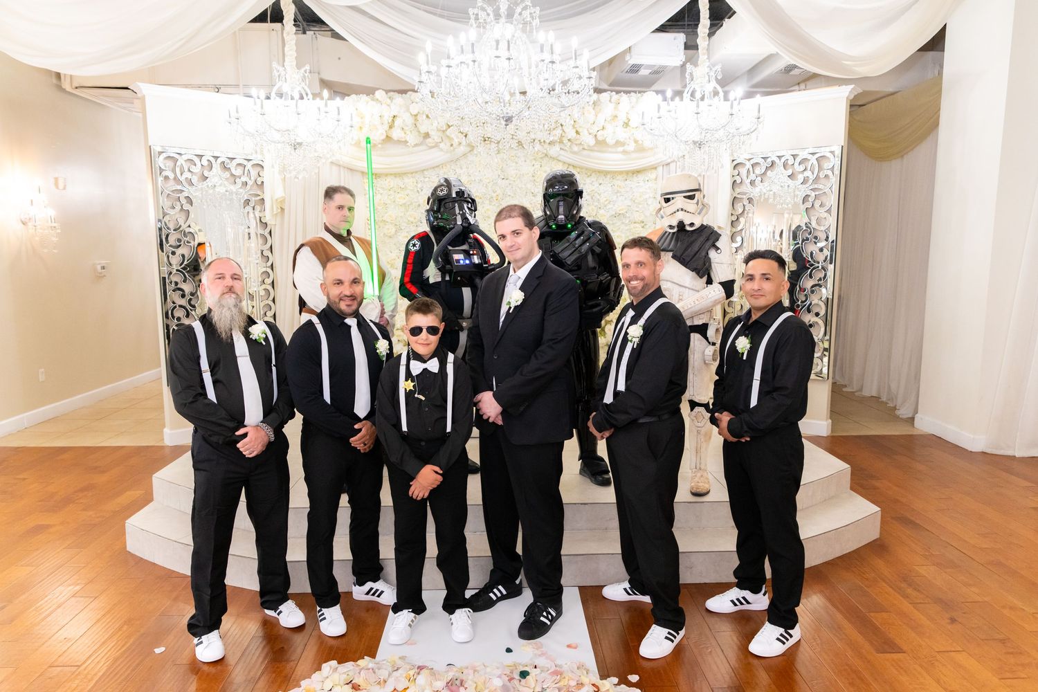 Groomsmen in black tuxedos pose with Star Wars characters at a themed wedding reception.