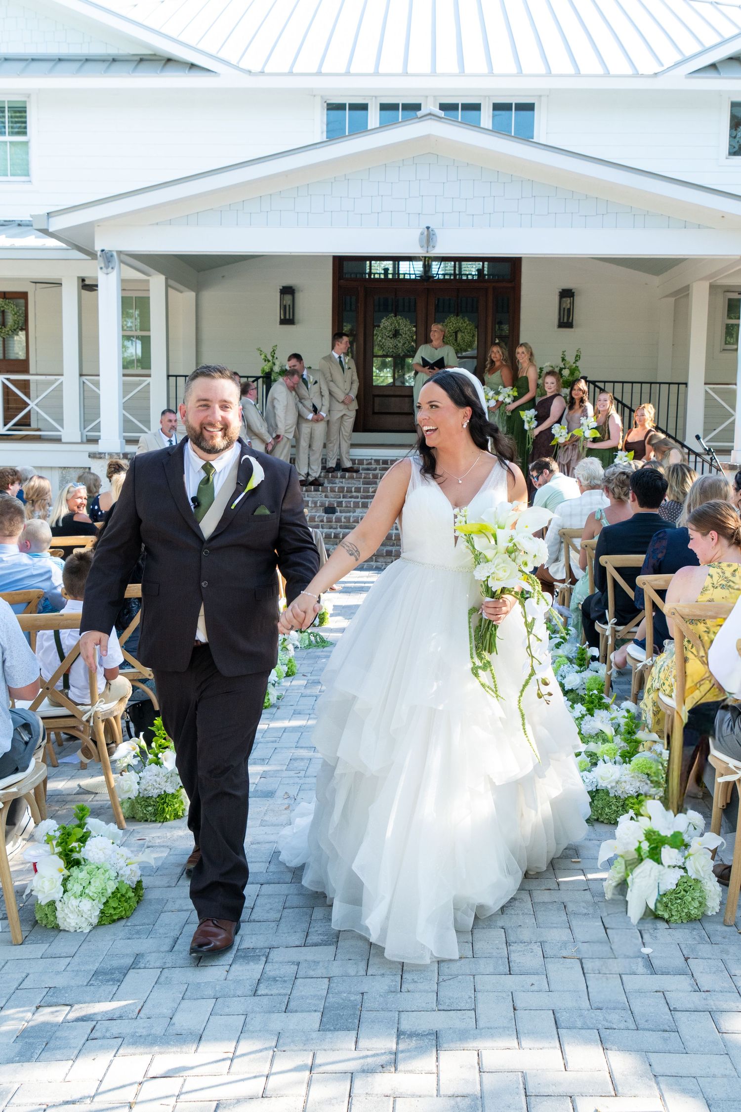 Newlywed couple holding hands walking down the aisle after outdoor wedding ceremony at white venue.