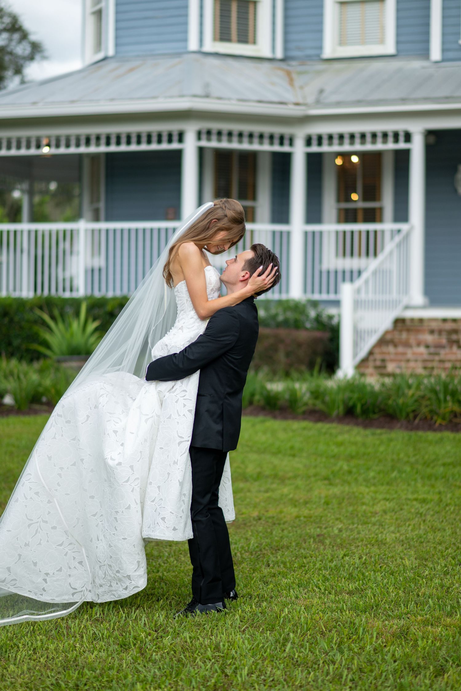 Groom lifting bride in elegant white wedding dress for a romantic kiss outdoors.
