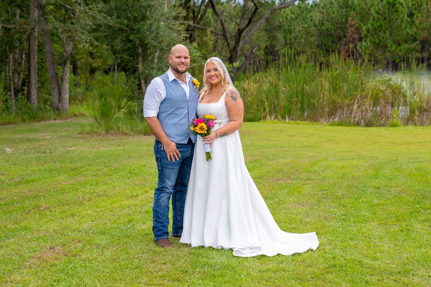 Bride and groom smiling together on green lawn with colorful bridal bouquet.
