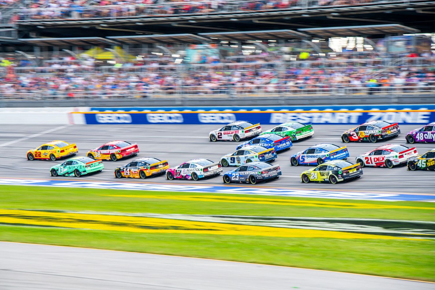 Large pack of colorful NASCAR race cars racing at Daytona International Speedway.