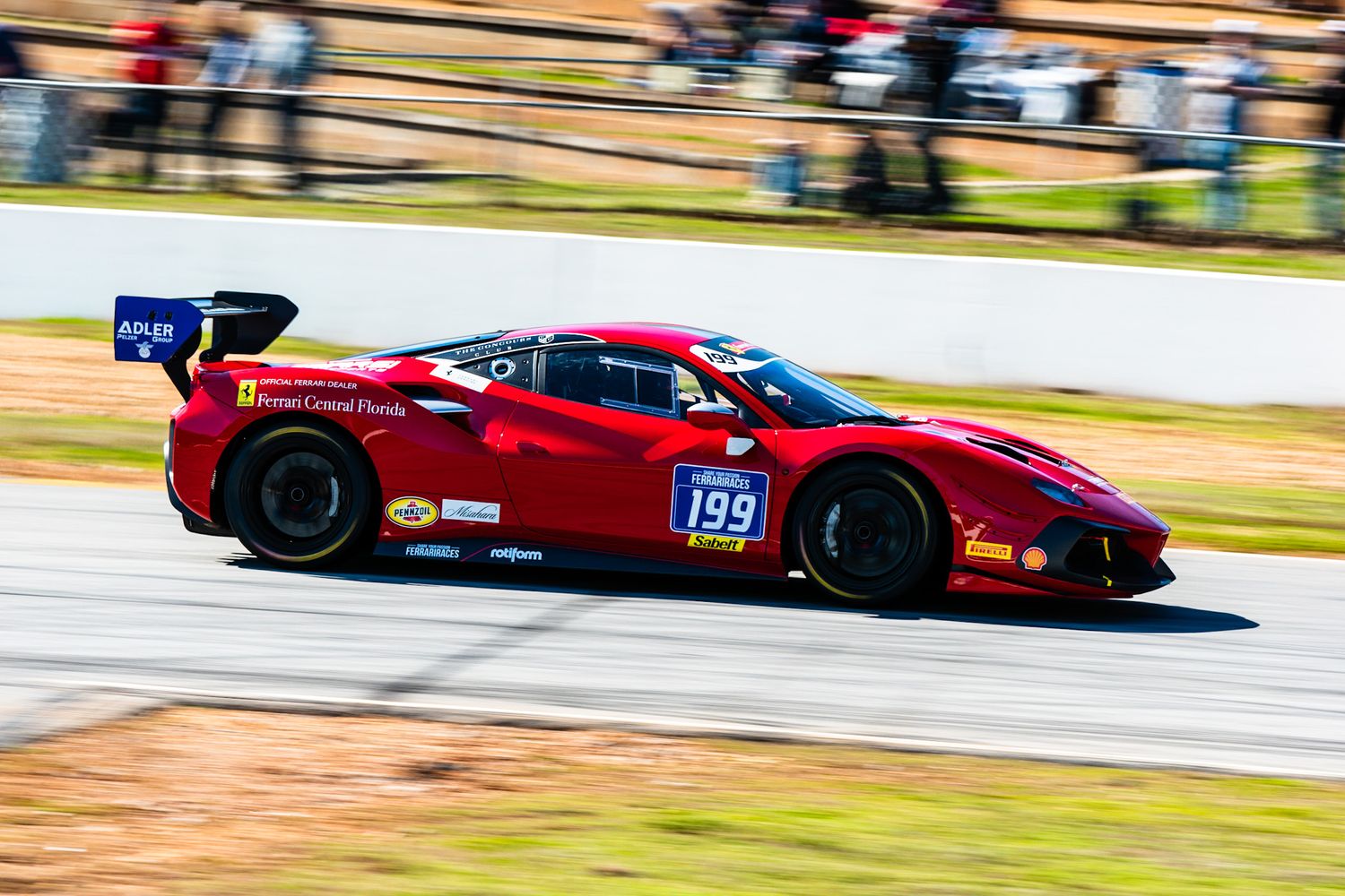 Red Ferrari 488 GT3 race car number J99 competing on a road course circuit.