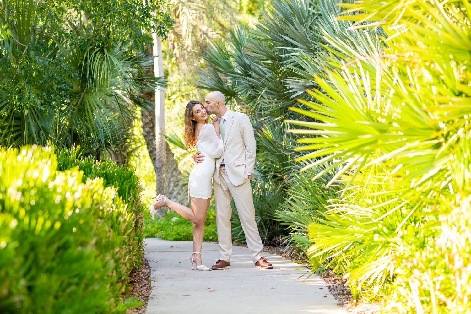 Happy couple embracing on a sunny garden path surrounded by lush tropical palm trees and greenery.